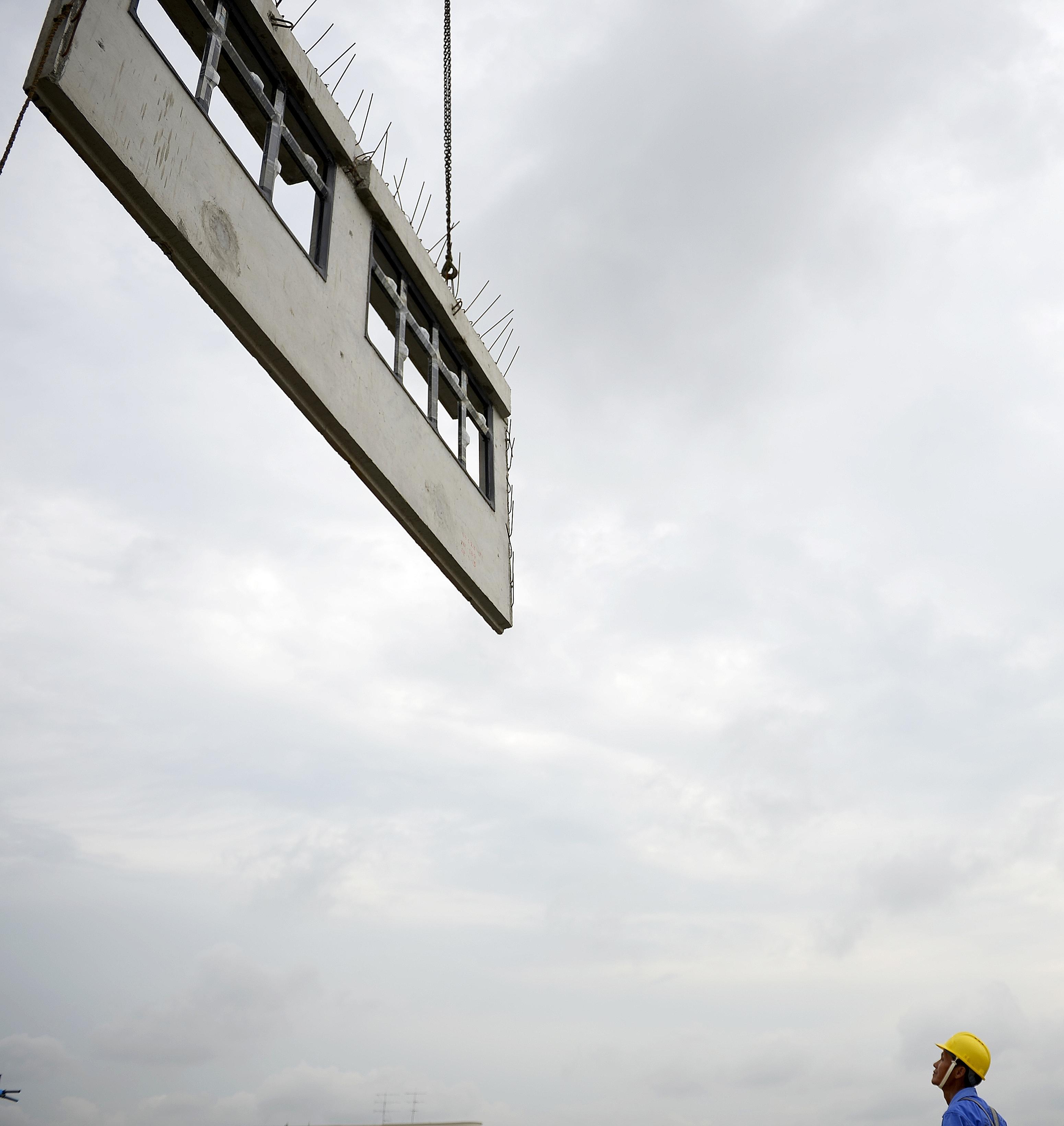 A tower crane lifting a precast facade wall into place on the 15th floor of the Hougang Crimson HDB project. 