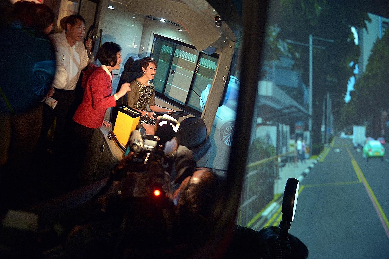 Senior Minister of State for Transport Josephine Teo testing one of the full-cabin simulators, as bus captain Amy Tan (in red) guides her along, at the new Bus Training and Evaluation Centre yesterday.