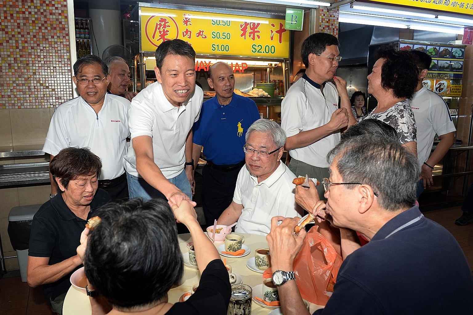 New PAP candidate Melvin Yong shaking hands and Mr Lui Tuck Yew talking to a resident during the walkabout at Pek Kio Market and Food Centre yesterday.