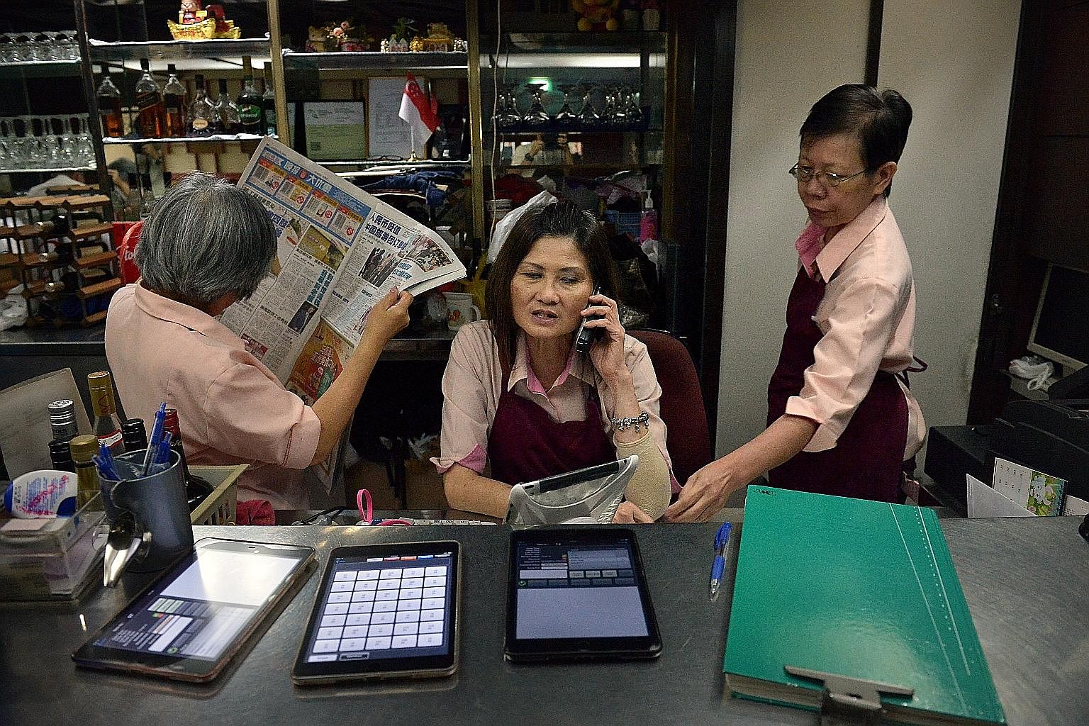 Ms Woon Ai Chun, 61, who has worked at the Shashlik restaurant for 11 years, prepares one of the restaurant's signature desserts, the Cherry Jubilee. Ms Jean Jee, 58, catches up on the news while Ms Wee Mui Quee (at right), 56, keeps herself busy as 