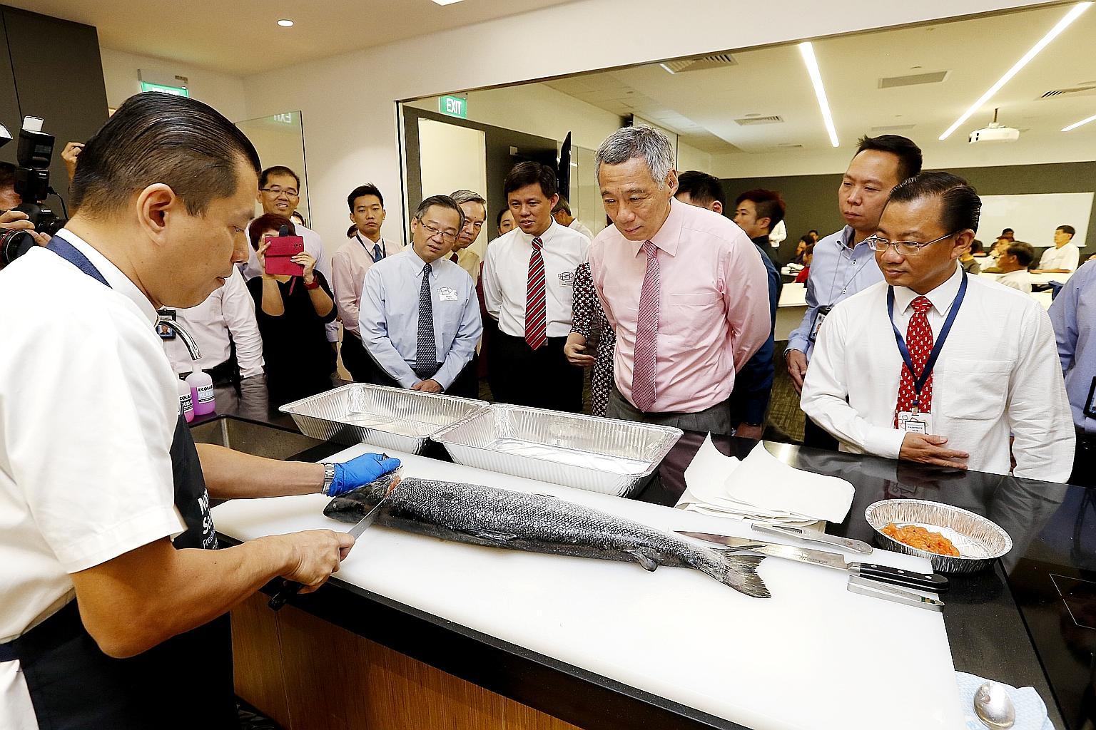 Prime Minister Lee Hsien Loong watching a fish being butchered at the new FairPrice Hub in Joo Koon yesterday. With him are Health Minister Gan Kim Yong (in blue with blue tie), labour chief Chan Chun Sing (with red striped tie) and NTUC FairPrice CE