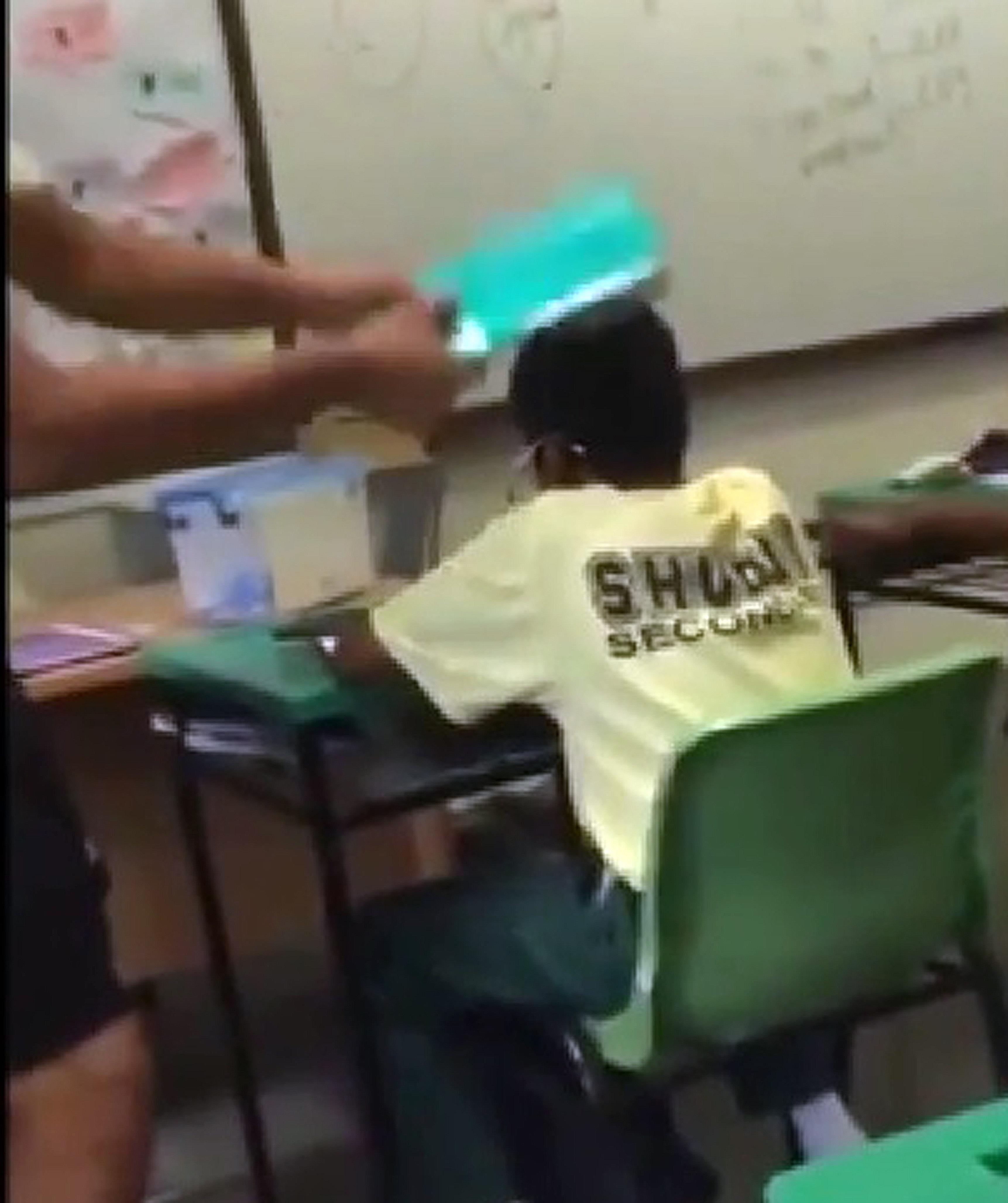 In the clip, two boys are seen keeping their heads bowed and not retaliating as another boy hits them on their heads repeatedly. Meanwhile, yet another boy is seen dancing on the teacher's table.