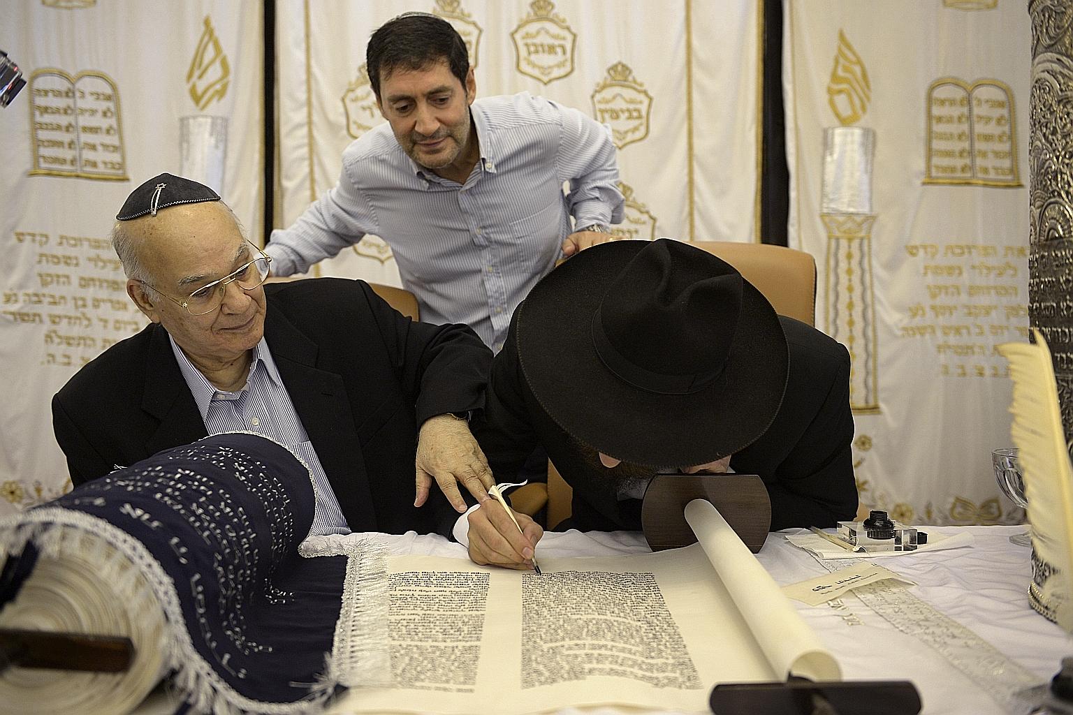 Mr Harry Elias (left) symbolically finishing the writing of a new set of Torah by holding on to the hand of Rabbi Mendy Goldshmid (right) as Mr Daniel Harel, who donated the set, watches. Rabbi Goldshmid, who is based in Koh Samui, flew here for the