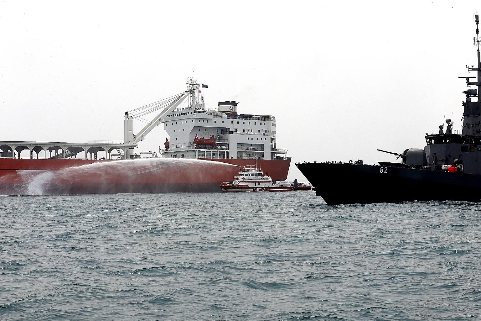 An SCDF maritime fire vessel dousing the FK Avatar cargo vessel (far left) with water after a patrol craft from the navy first alerted multiple agencies under the SMCC to the presence of "hijacking" activities.