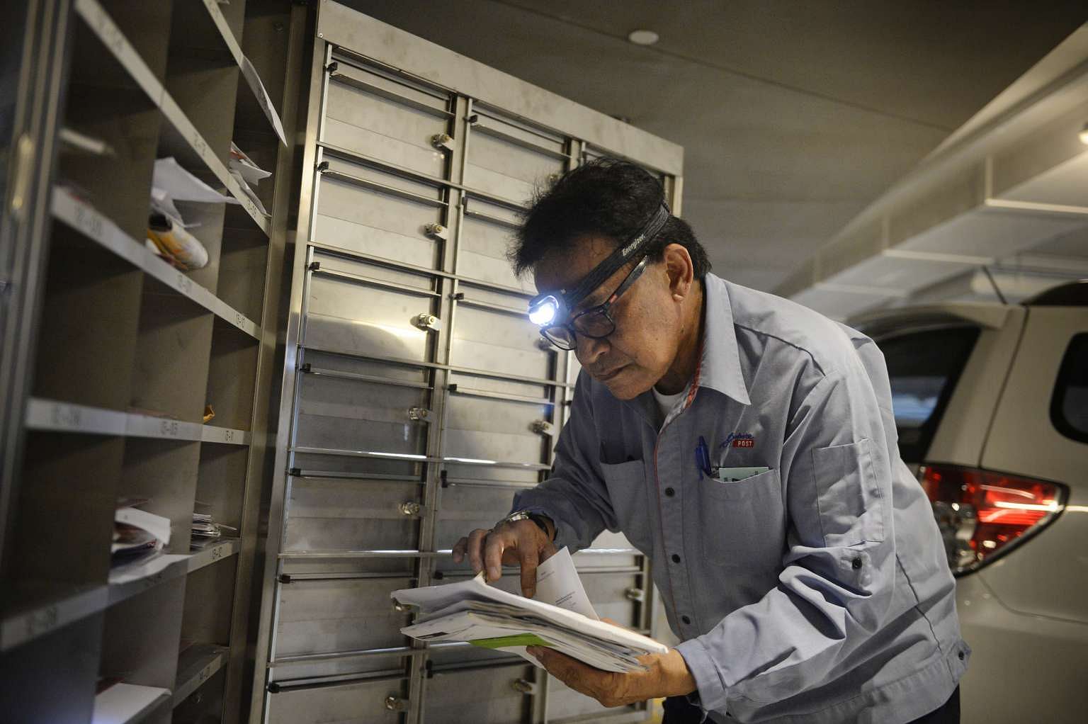 Postman Salim Nahrawi, 69, delivering letters at a building in Tanjong Pagar. The head light helps improve visibility.
