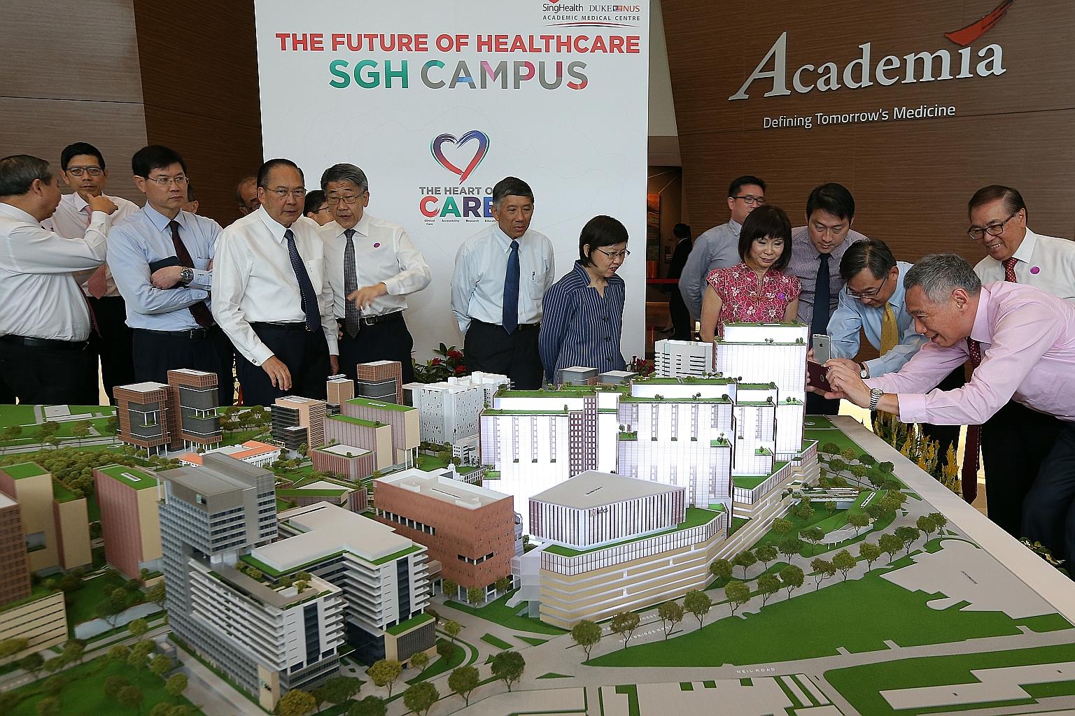 Prime Minister Lee Hsien Loong (right) and Health Minister Gan Kim Yong snapping photos of a model of SGH's campus masterplan yesterday. With them is Senior Minister of State for Health Amy Khor (in pink). More space will be given to areas where the