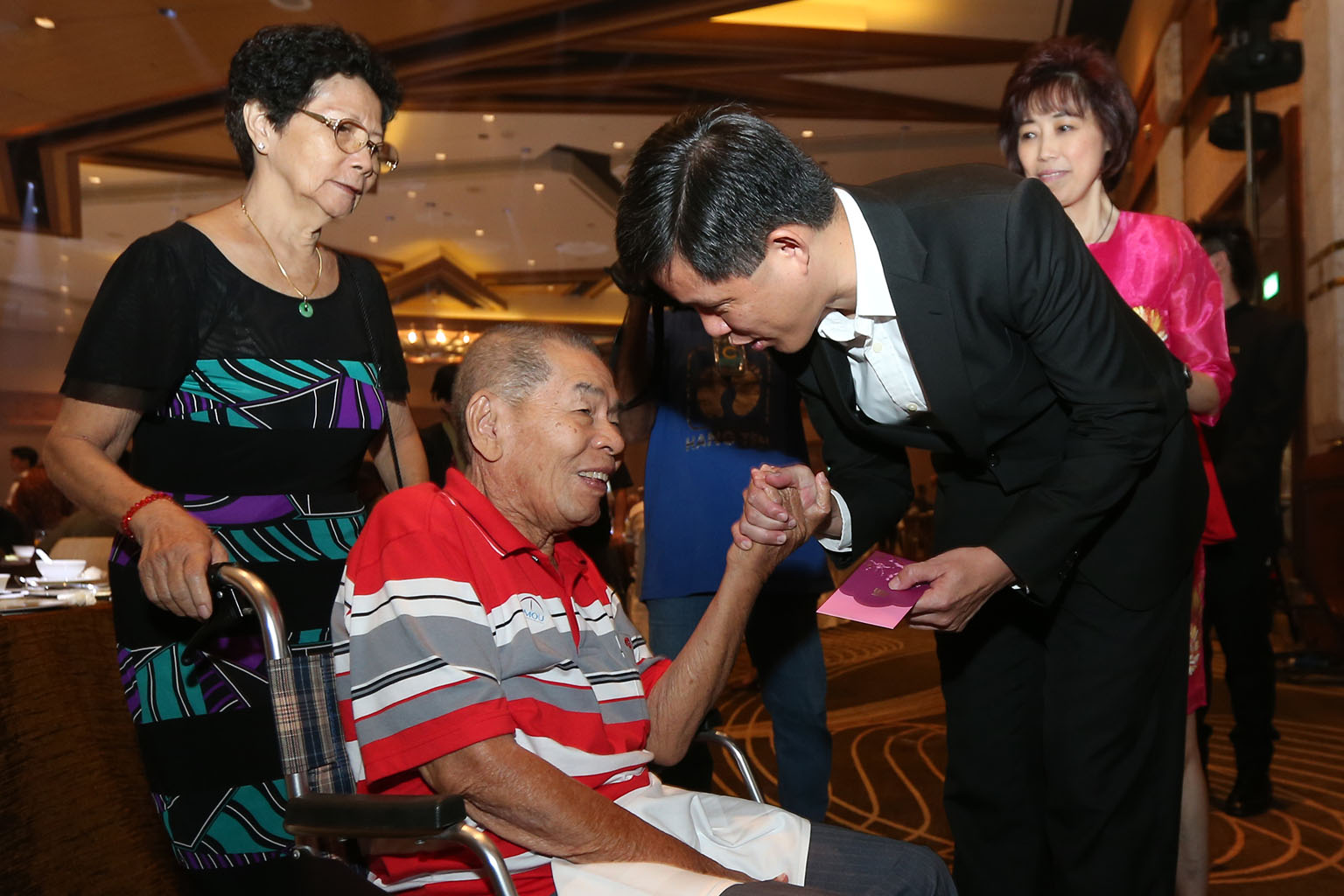 NTUC secretary-general Mr Chan presenting a red packet to Mr Leo, a former marine chief engineer and SMOU member, who is accompanied by his wife, Madam Dan (left), during the SMOU 65th anniversary Chinese New Year luncheon and hongbao presentation yesterd