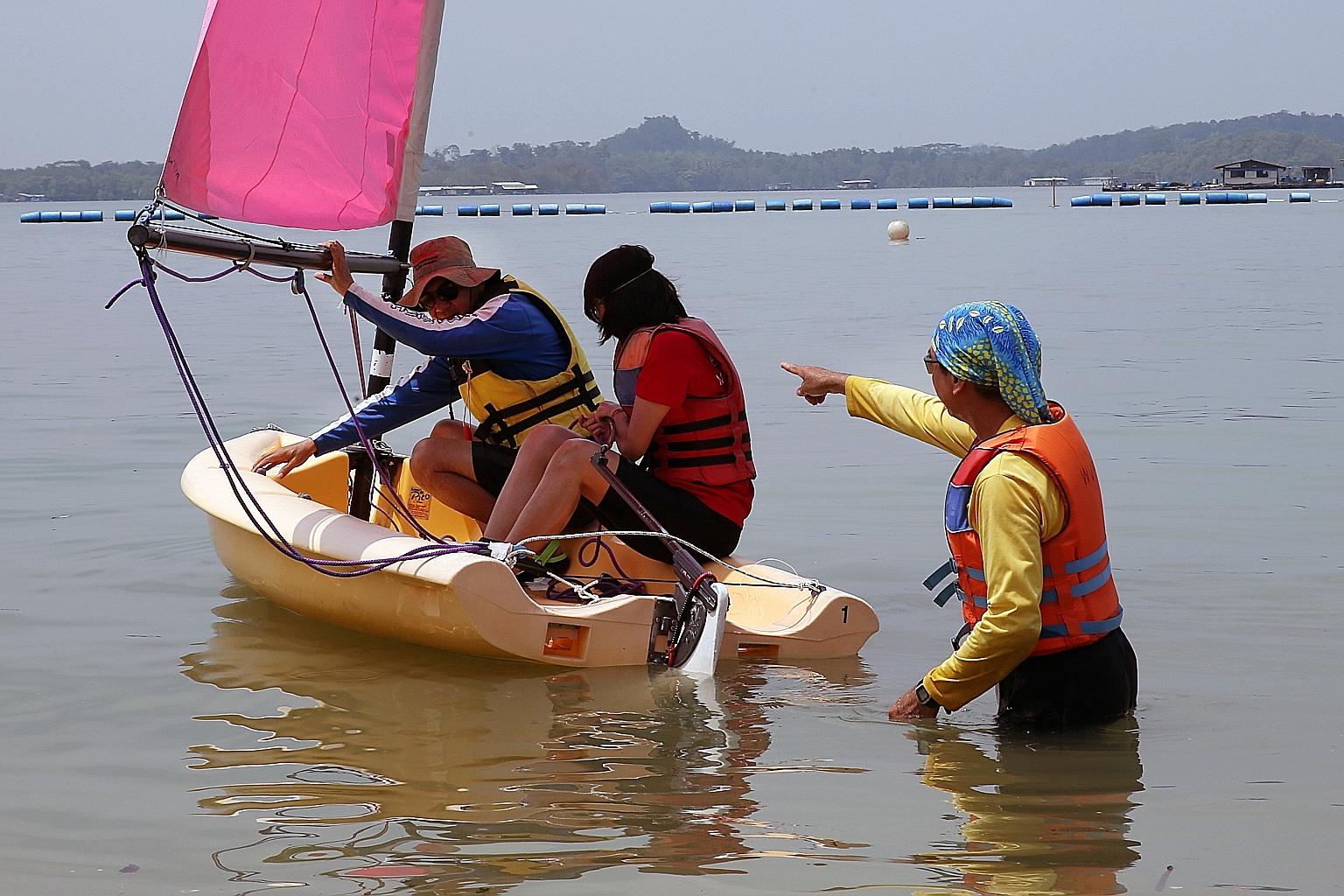 Volunteer trainer James Leong in the water assisting a fellow instructor on the sailboat in guiding one participant of the sailing certification course on how to manoeuvre the craft.