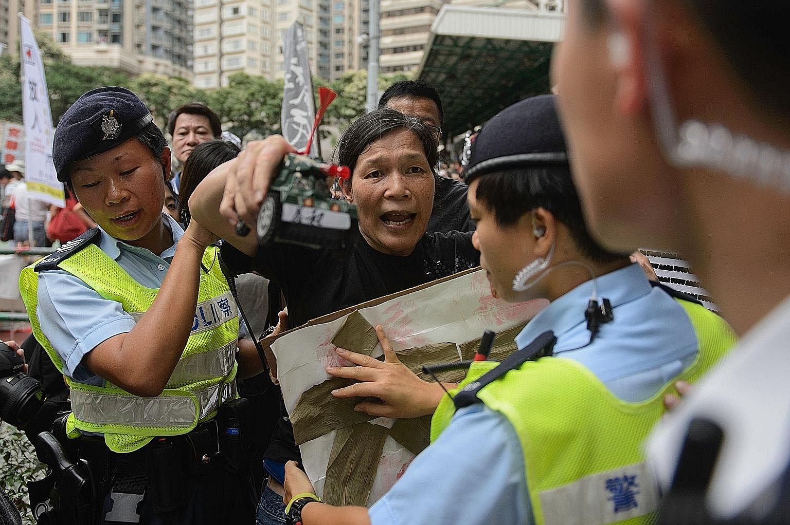 Police holding back a pro-democracy activist, with a toy tank in her hand, after she taunted pro-China demonstrators in Hong Kong on Sunday. The pro-China demonstrators had gathered to counter-protest against a pro-democracy rally ahead of the annive