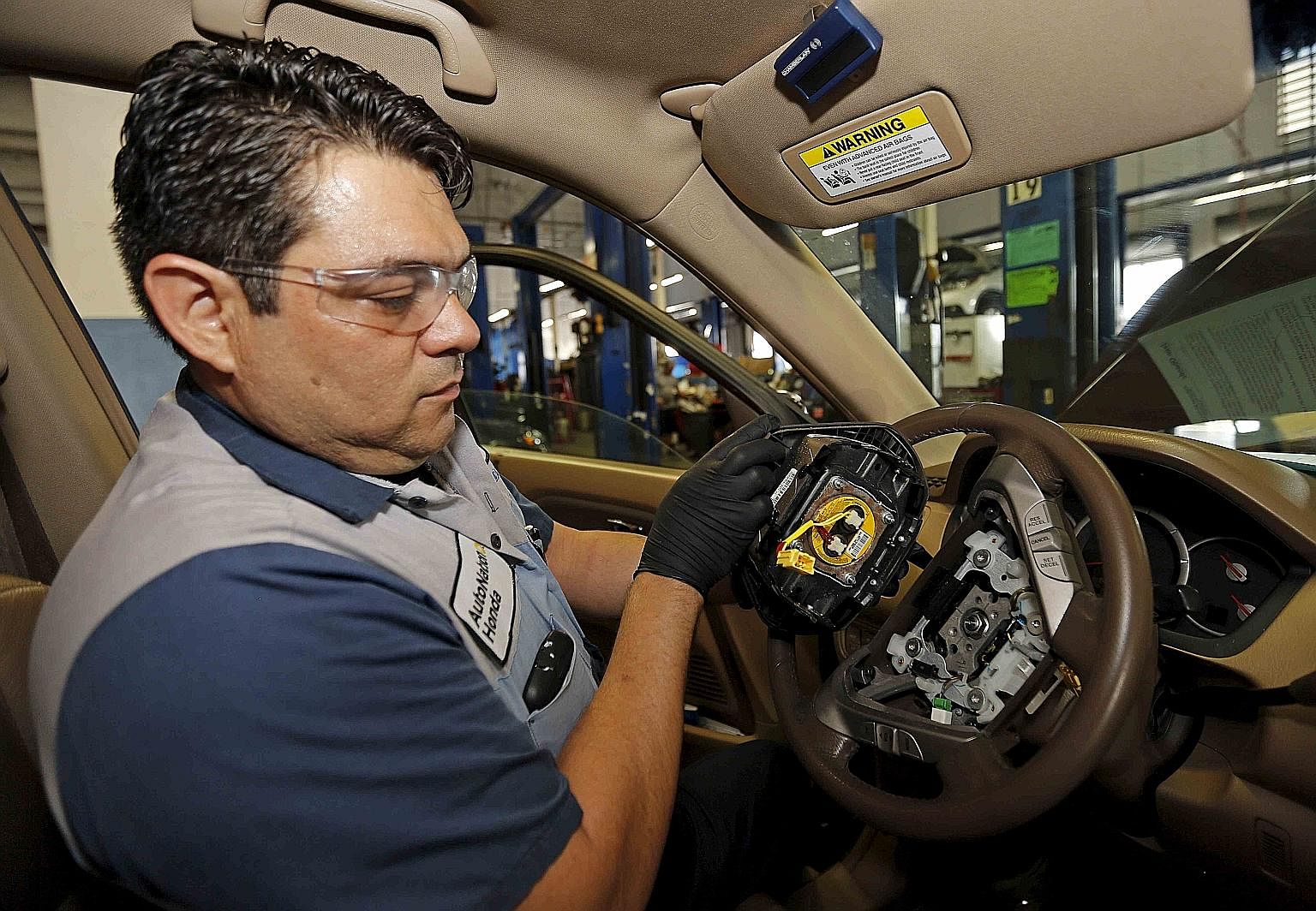 Technician Edward Bonilla holding a recalled Takata airbag inflator after removing it from a Honda car at a dealership service department in Miami, Florida.