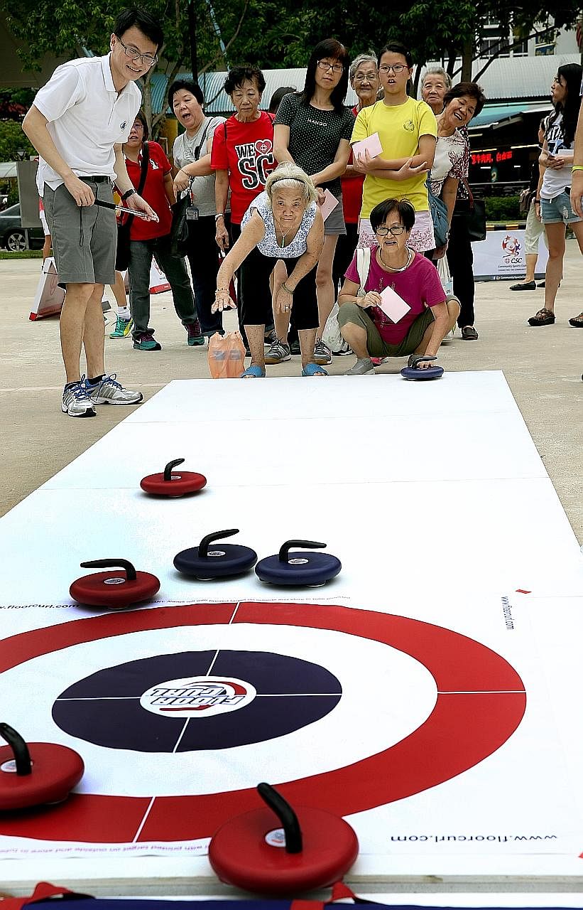 Madam Margaret Lee, 71, (squatting) and Madam Kok Ee San, 78, try out floor curling at a Community Sports Day event held yesterday. The sports day aims to promote racial harmony.
