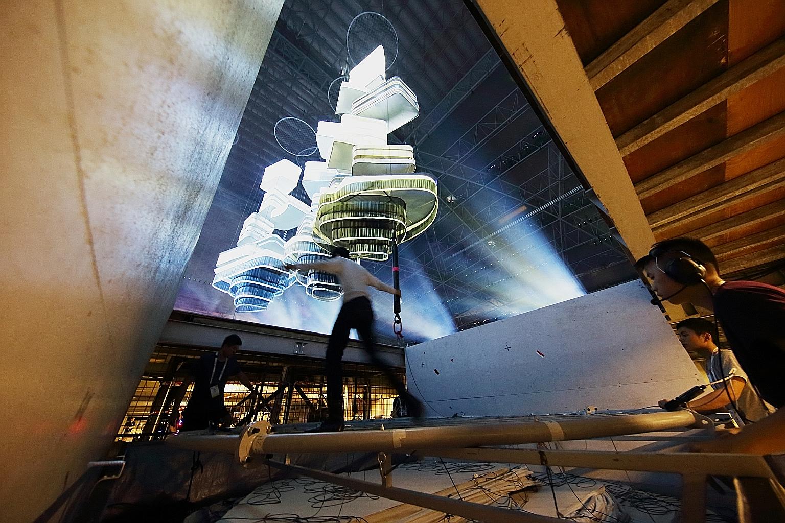 Ground crew below the stage at the National Stadium preparing to raise one of the clusters of the Sky City through the trapdoor during a rehearsal for the Parade. Three other clusters are already in the air, illuminated by powerful projectors.