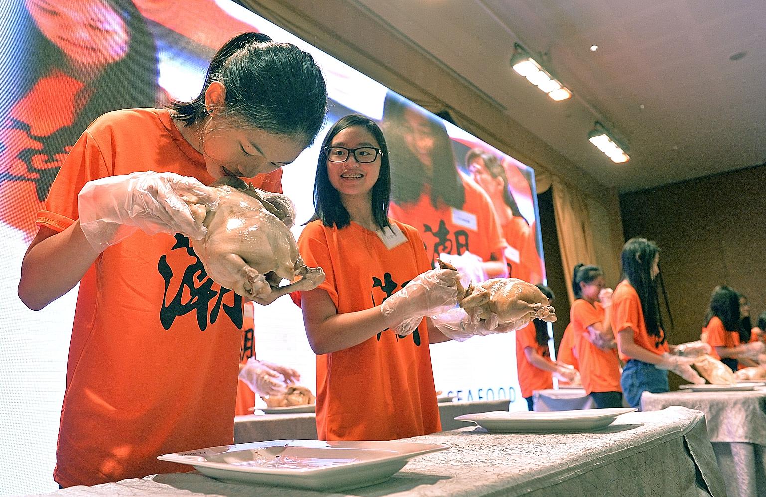 Student Geena Ang having a go at a rooster's head, alongside her schoolmate Andrea Chua, while taking part in the ancient Teochew coming-of-age ritual known as Cu Huay Hng at Chui Huay Lim Club yesterday.