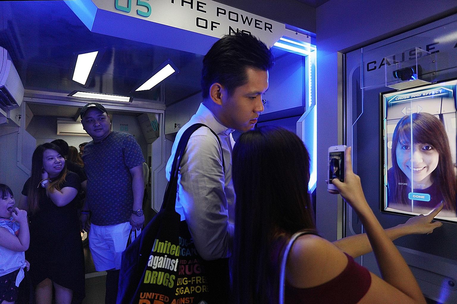 Visitors on board the "Drug Buster Academy Bus" at CNB's one-day roadshow at VivoCity yesterday. This special bus makes use of augmented reality technology to transform people's faces so they can see for themselves what drugs can do to them.