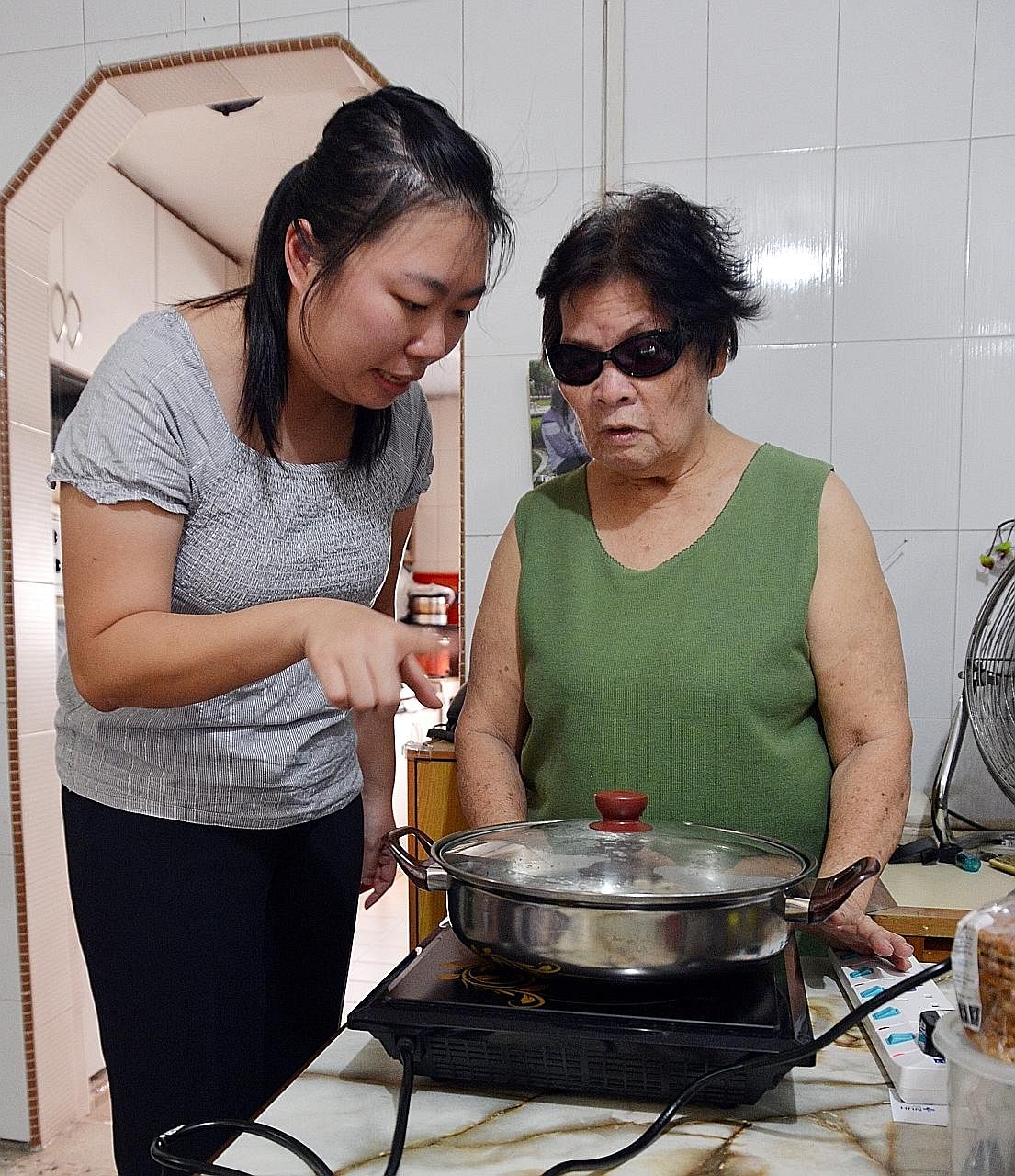 Senior occupational therapist Chen Xuanyu shows housewife Joy Leong how to cook food and boil water more safely. Madam Leong has total vision loss in one eye and partial vision in the other.