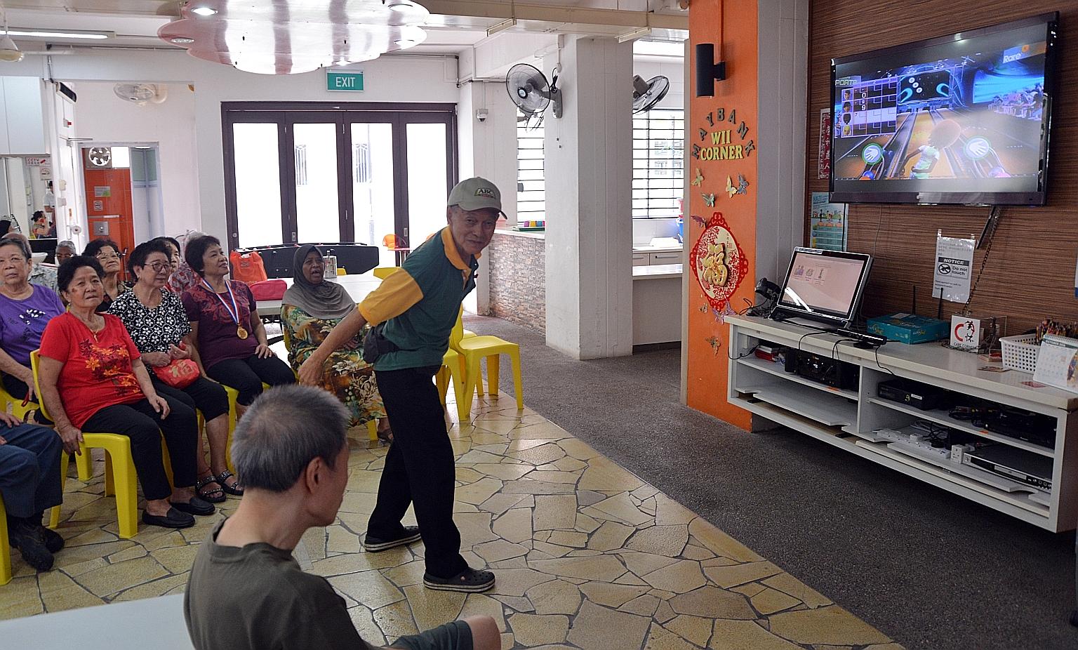 Mr Eng (centre) striking a pose while playing Kinect Bowling at the senior activity centre at the void deck of Block 170 in Lorong 1, Toa Payoh. The activity is held every Thursday from 10am to noon, and about 16 people are selected to play. Voluntee