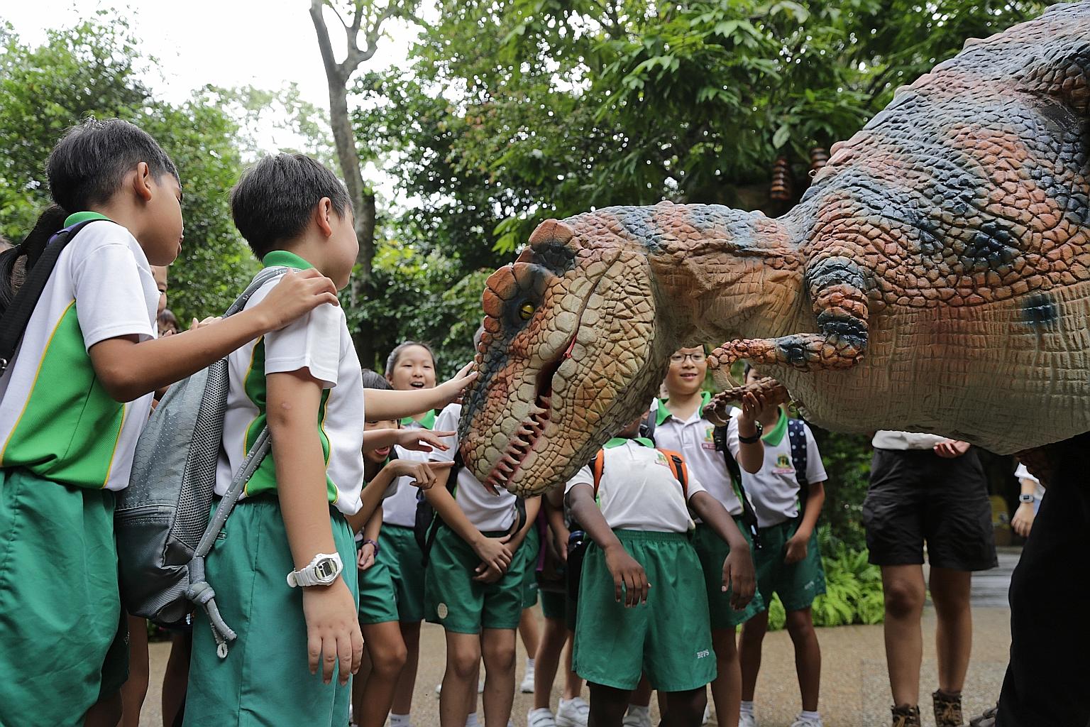 Students interacting with a T-rex mascot at the entrance to Dinosaur Valley - Singapore Zoo's latest attraction, which features lifelike animatronics of 16 dinosaur species including Tyrannosaurus rex and Spinosaurus. The exhibit seeks to raise aware