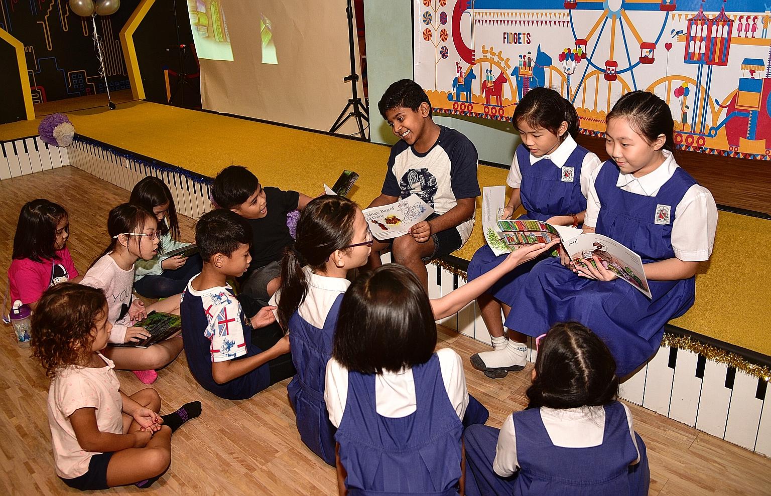 Twelve-year-old Joash Marcus Daniel (left), a beneficiary of The Business Times Budding Artists Fund, reading aloud to a group of young children along with two 10-year-old authors - Amanda Toh and Shanyce Goh (right). Both girls, who are from CHIJ Ke
