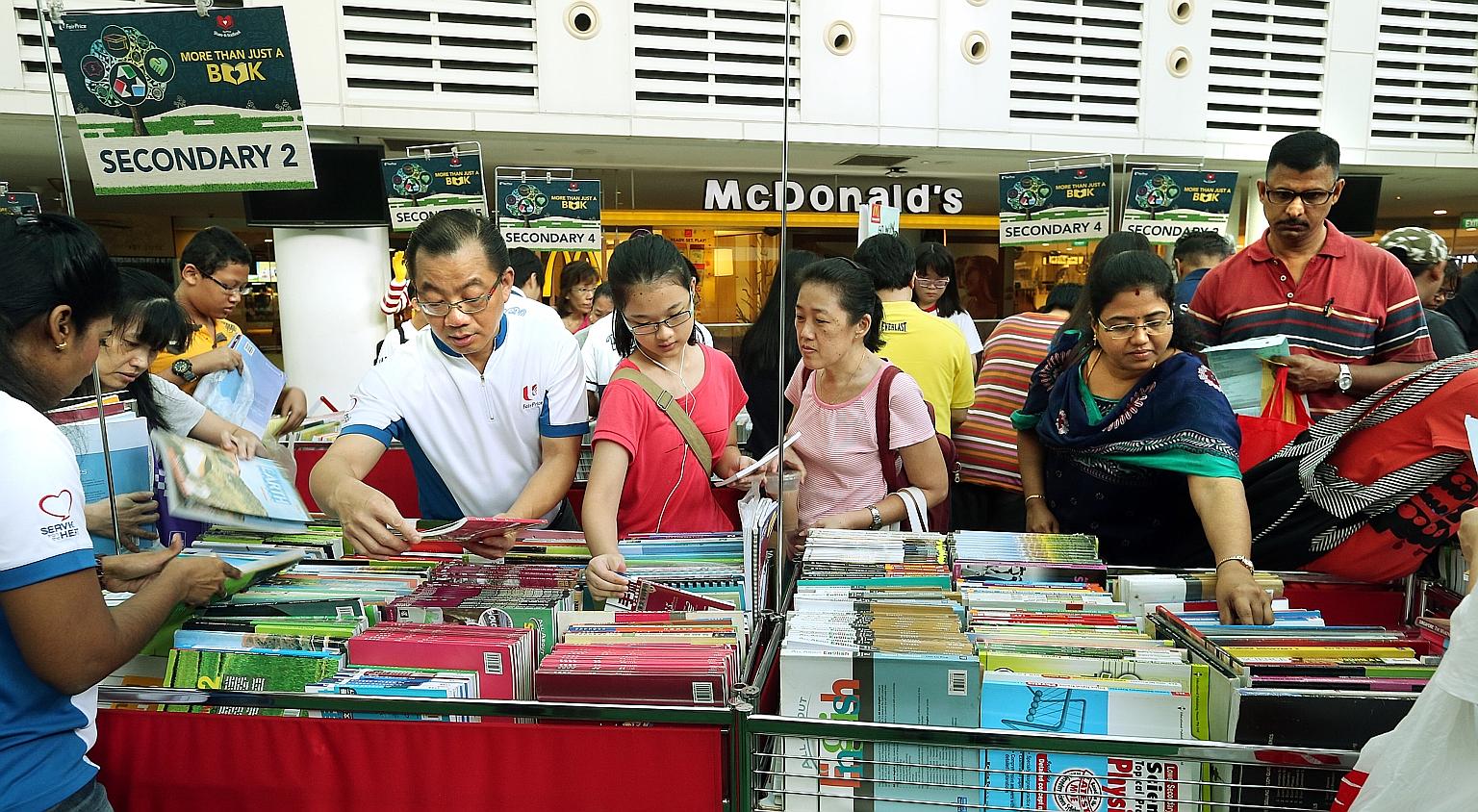 Mr Seah (left) looking at school books with parents and caregivers at the City Square Mall distribution point yesterday.