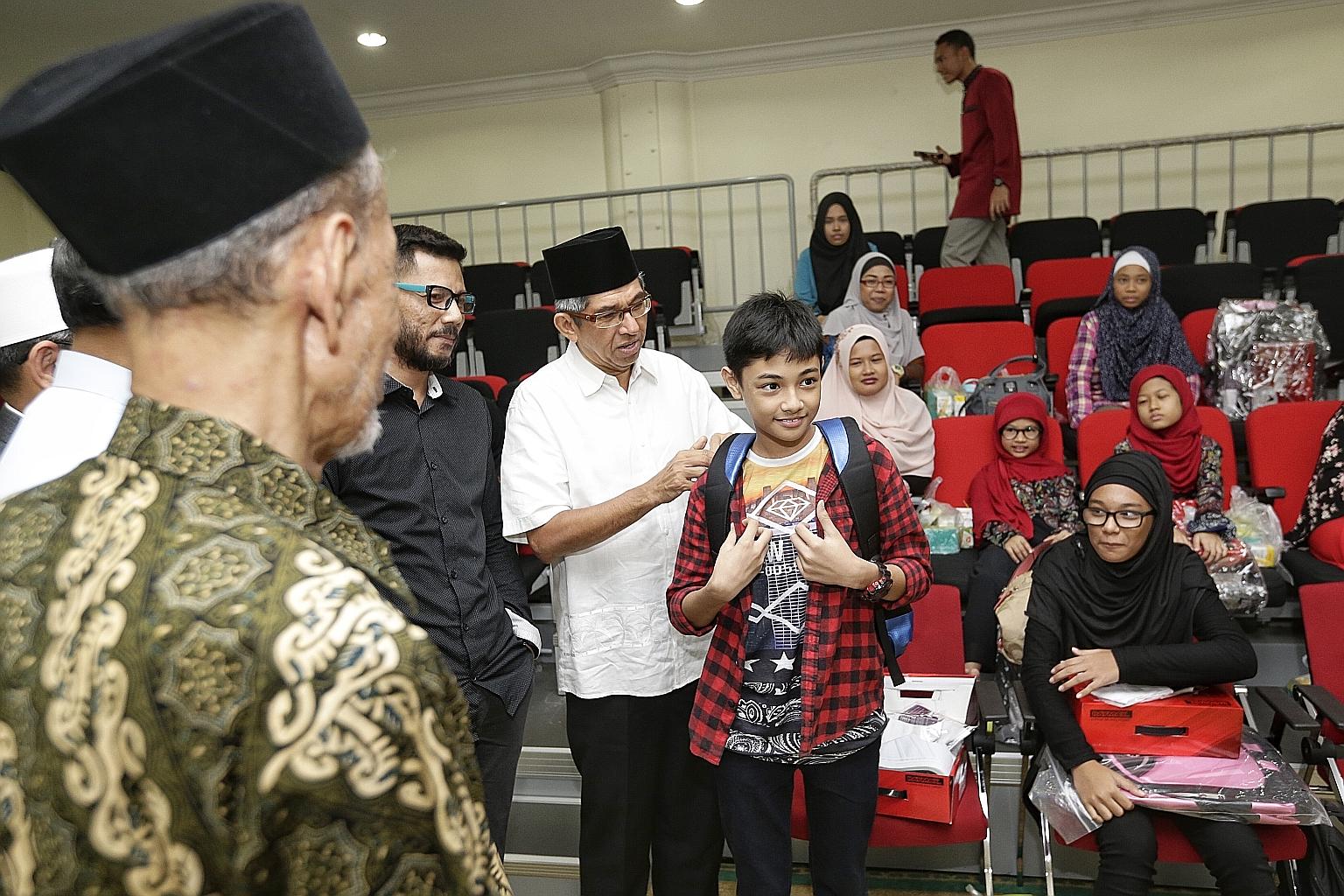 Dr Yaacob helping Raisyad Danish Imran, 12, yesterday with his new school bag, which is part of a back-to-school pack for beneficiaries.