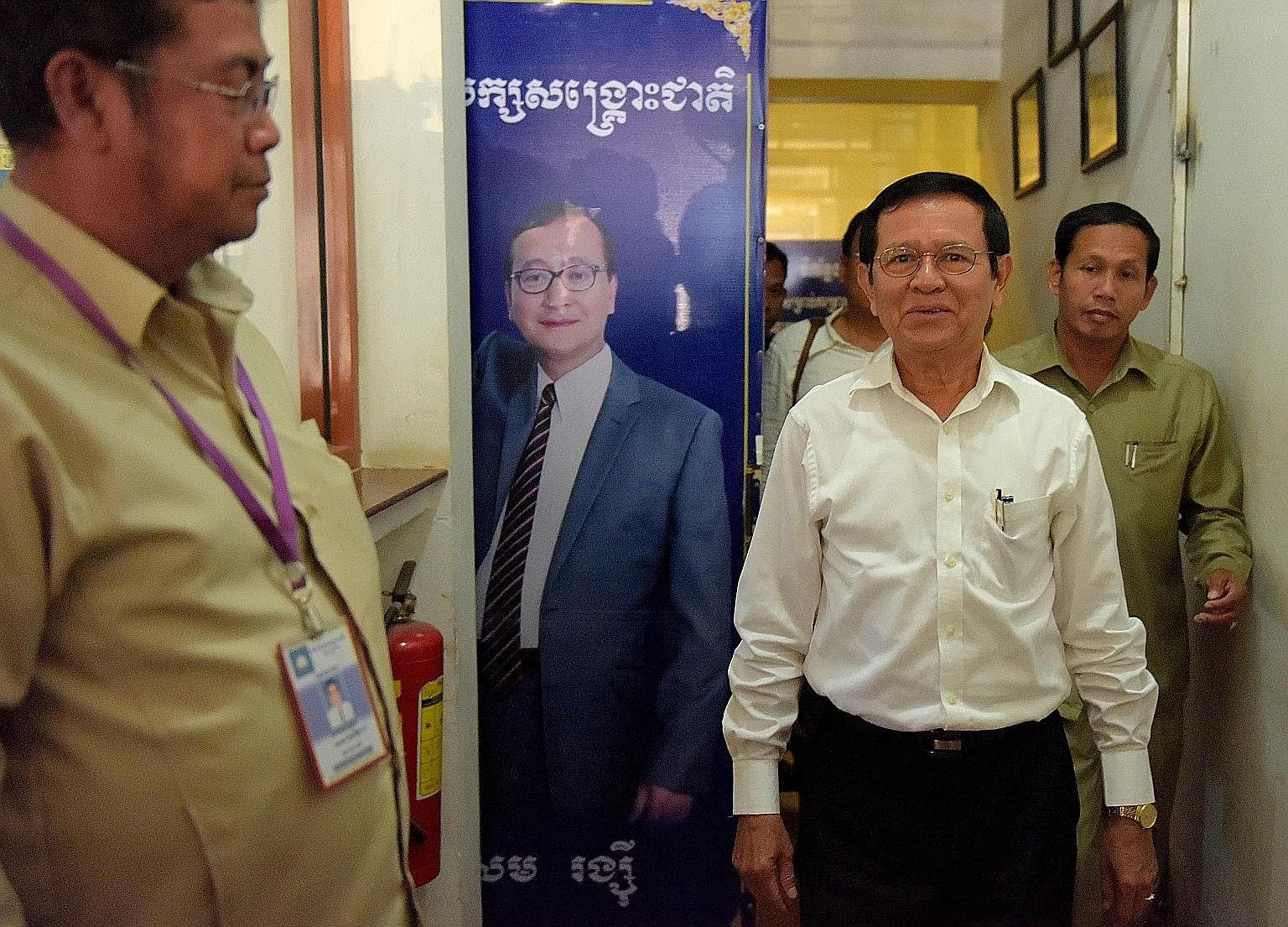 CNRP acting president Kem Sokha (in white shirt) walking past a portrait of exiled leader Sam Rainsy, who resigned as president of the opposition party recently, at its headquarters in Phnom Penh on Sunday. CNRP, Cambodia's leading opposition party, 