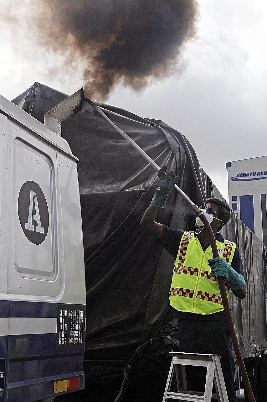 Mr Ganesan Naransamy, 27, an auxiliary police officer sticking a probe into the exhaust pipe of a lorry yesterday. The probe is connected to a Hartridge Smoke Meter, which measures the opacity of smoke emitted.