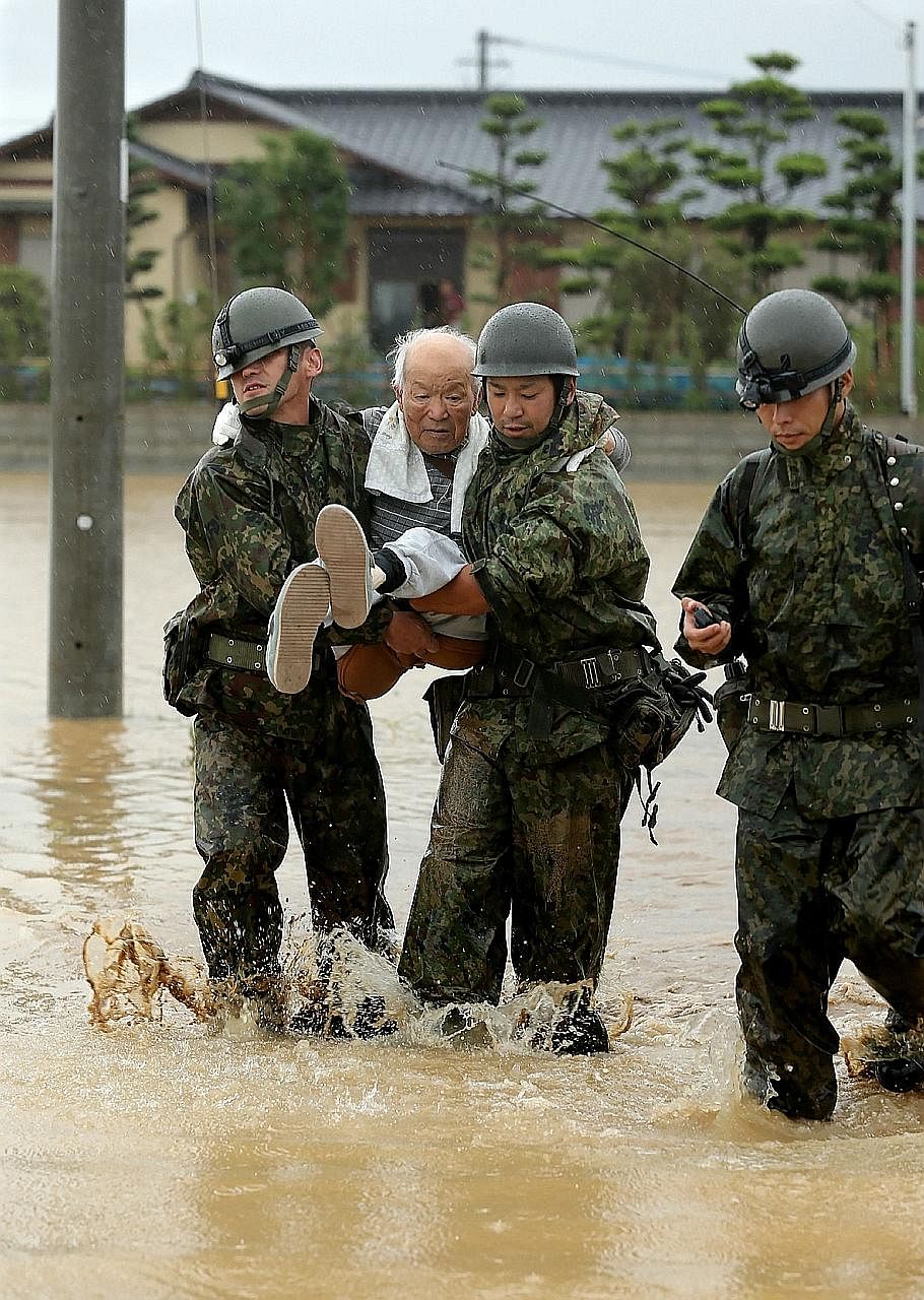 Right: Asakura City in Fukuoka prefecture is among the hardest-hit areas, with footage showing floodwaters surging through the streets yesterday. Above: These soldiers rescuing an elderly man in Asakura were among thousands of police officers and tro