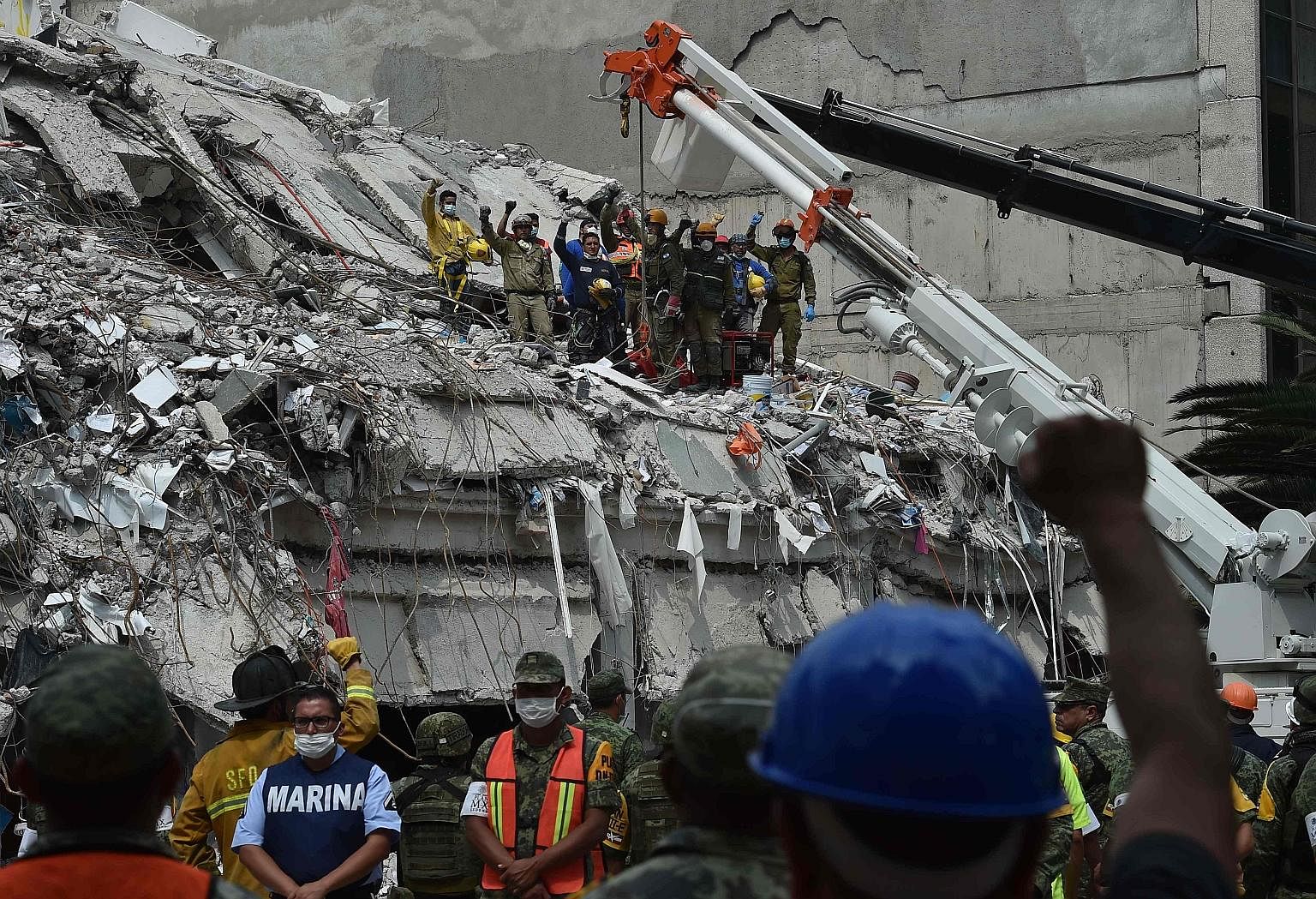 Rescuers and firefighters raising their fists to pay their respects to a man who survived the quake but died before they could reach him during their search for survivors at a flattened building in Mexico City on Thursday.