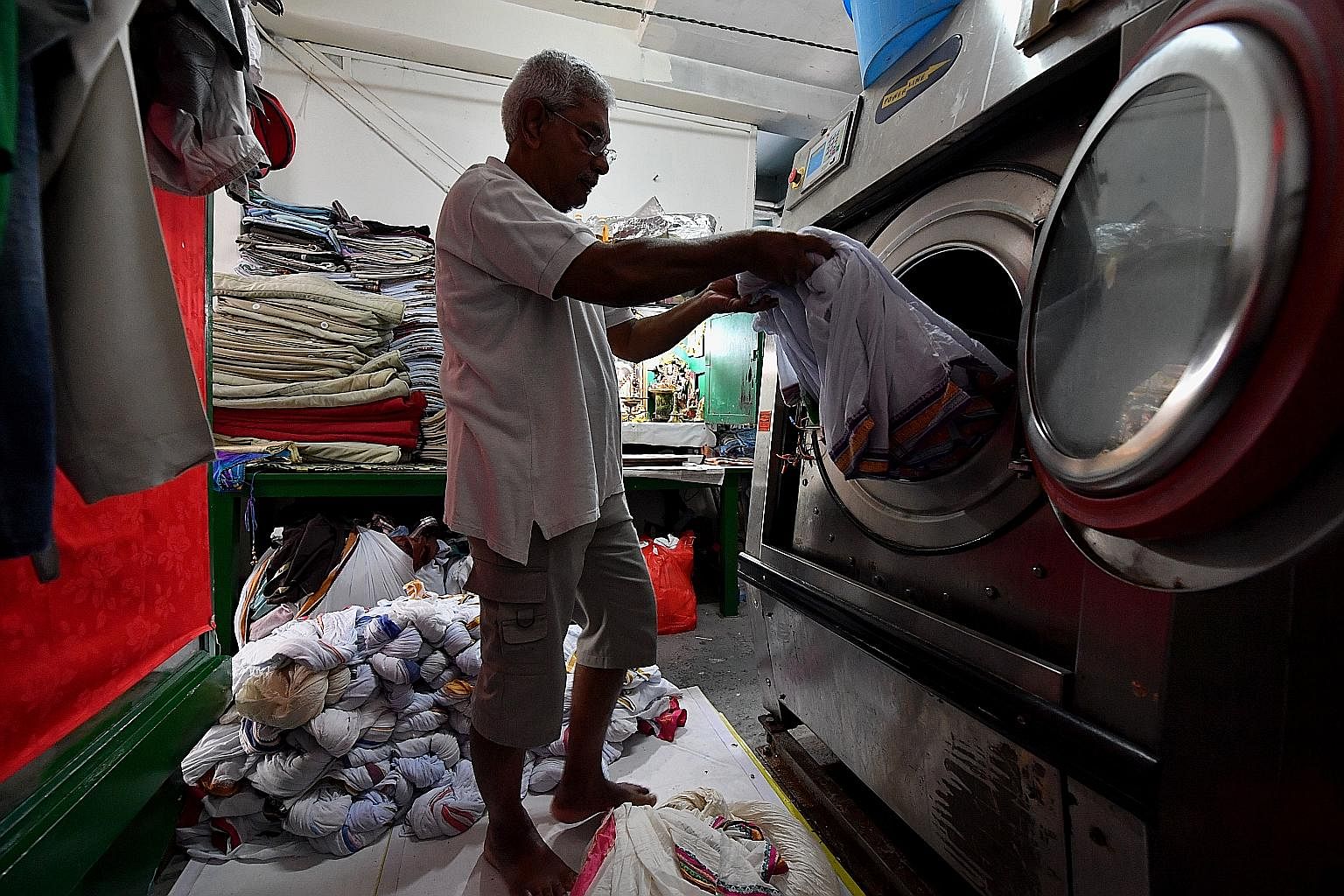 Mr Sambasivam unloading freshly washed laundry to be starched and dried later. The 73-year-old is a family friend who helps out in the shop, doing mainly administrative work. Left: After starching, the white dhotis are soaked in a pail of water with 