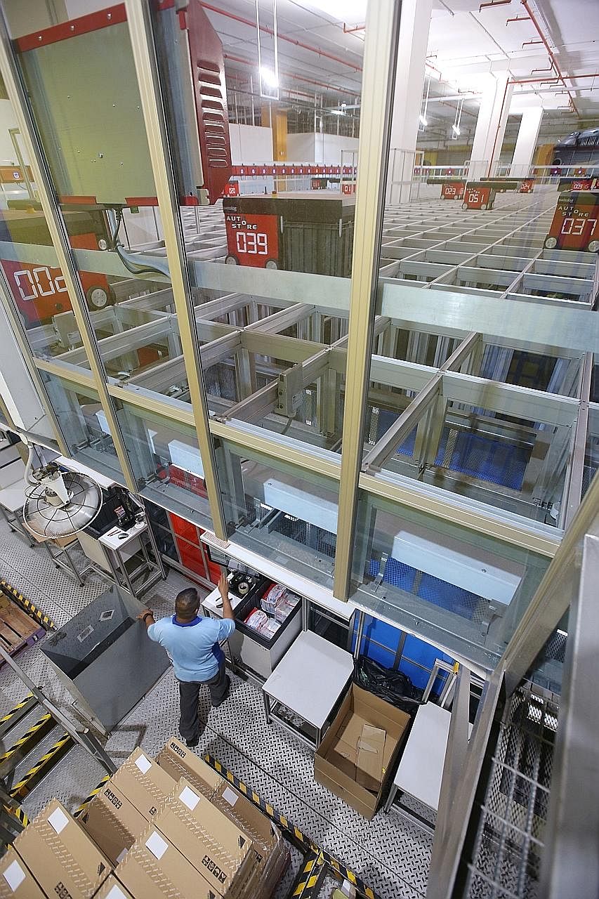 A worker at the FairPrice Hub distribution centre loading a bin with items for storage. The new automated storage and retrieval system brings bins containing order items to employees stationed at picking bays, where they bag and dispatch items for de