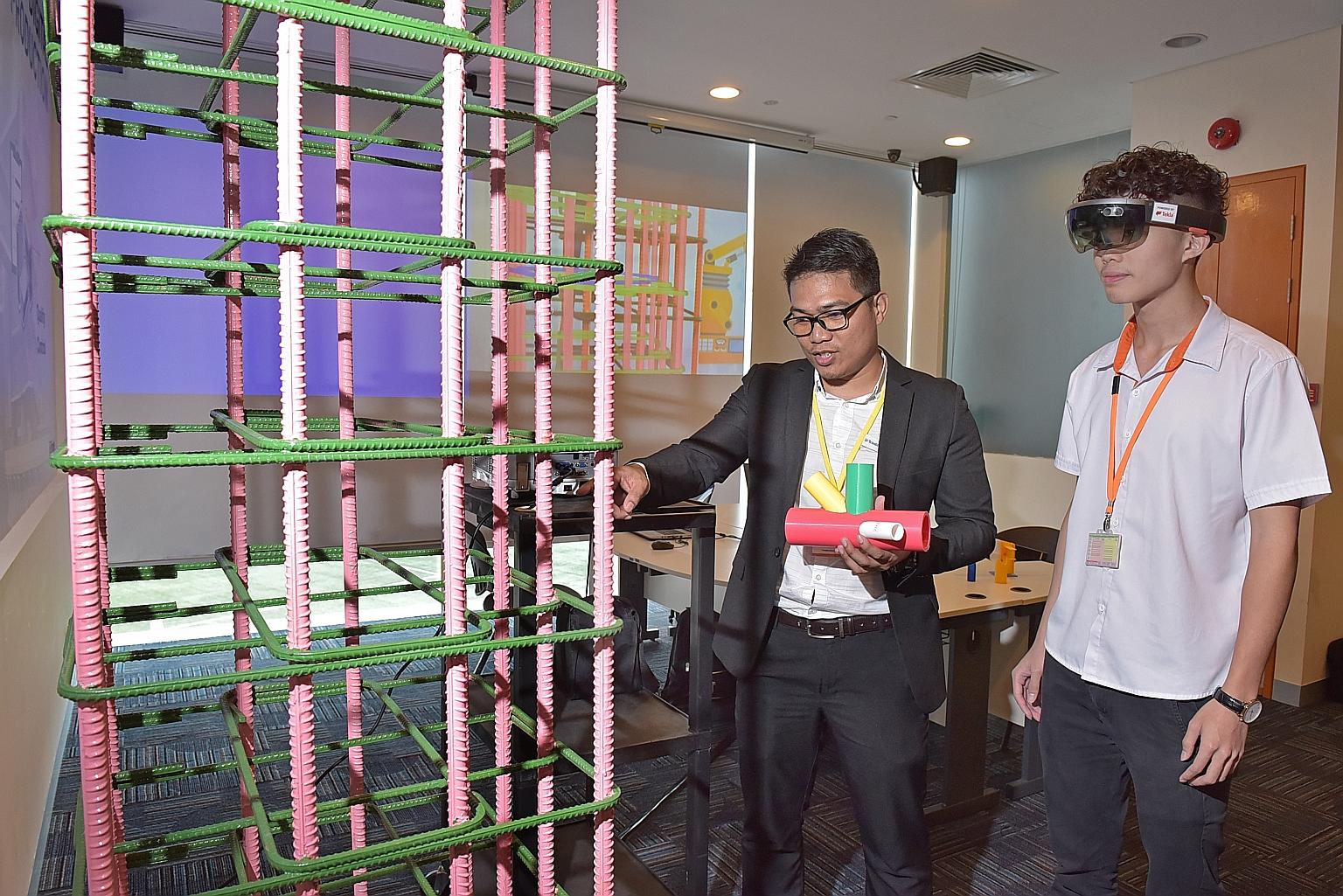 ITE civil and structural engineering design student Chia Jia Han (right) wears a hololens device to inspect a physical model against a virtual model under Trimble technical specialist Marvin Garcia's guidance at the Integrated Digital Delivery centre