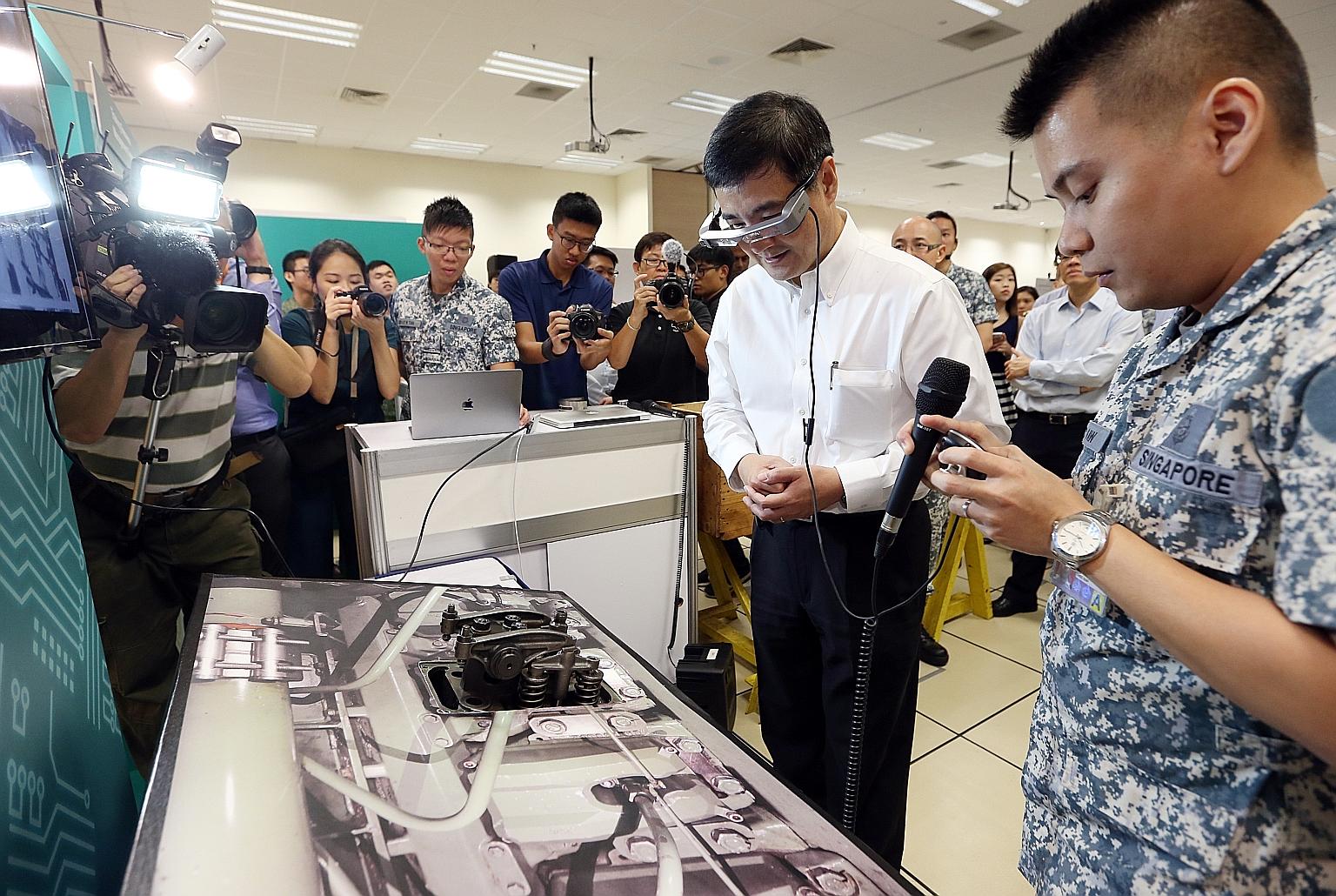 Senior Minister of State for Defence Heng Chee How trying out a smart maintenance system using augmented reality with the help of Military Expert 5-1 Aw Chee Giap (right) yesterday.