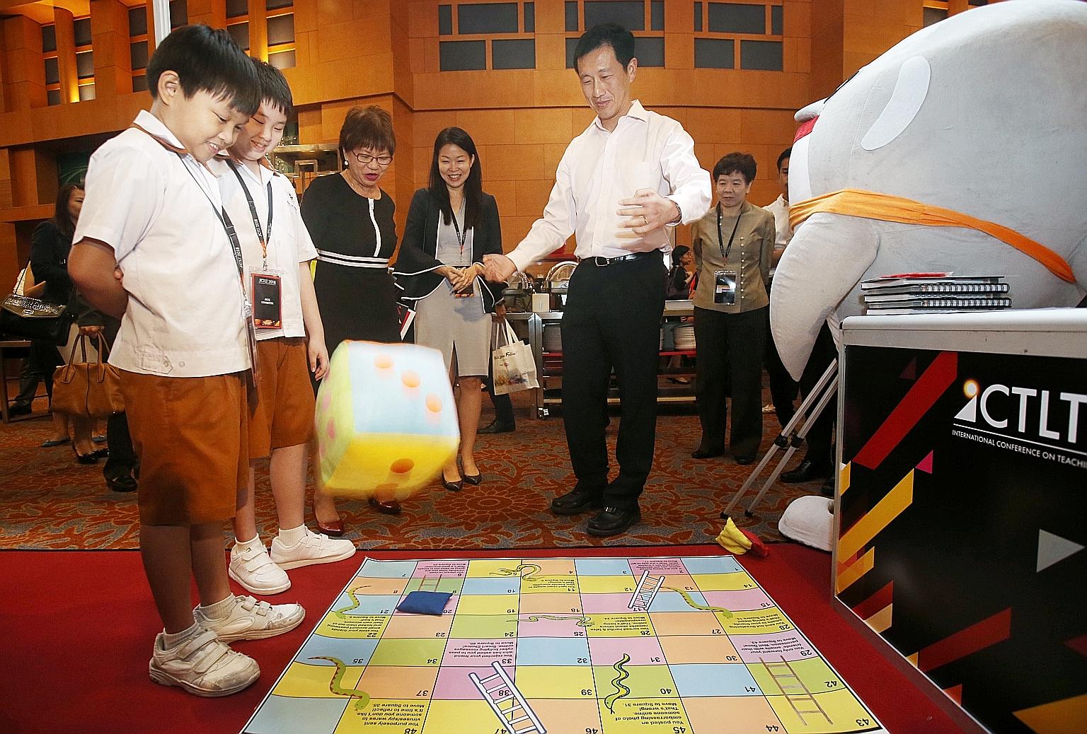 Education Minister Ong Ye Kung throwing a dice as he played a game of snakes and ladders focused on the theme of cyber wellness, created by Ahmad Ibrahim Primary School pupils Austin Kho (left) and Loo You En (second from left), and their teachers. W
