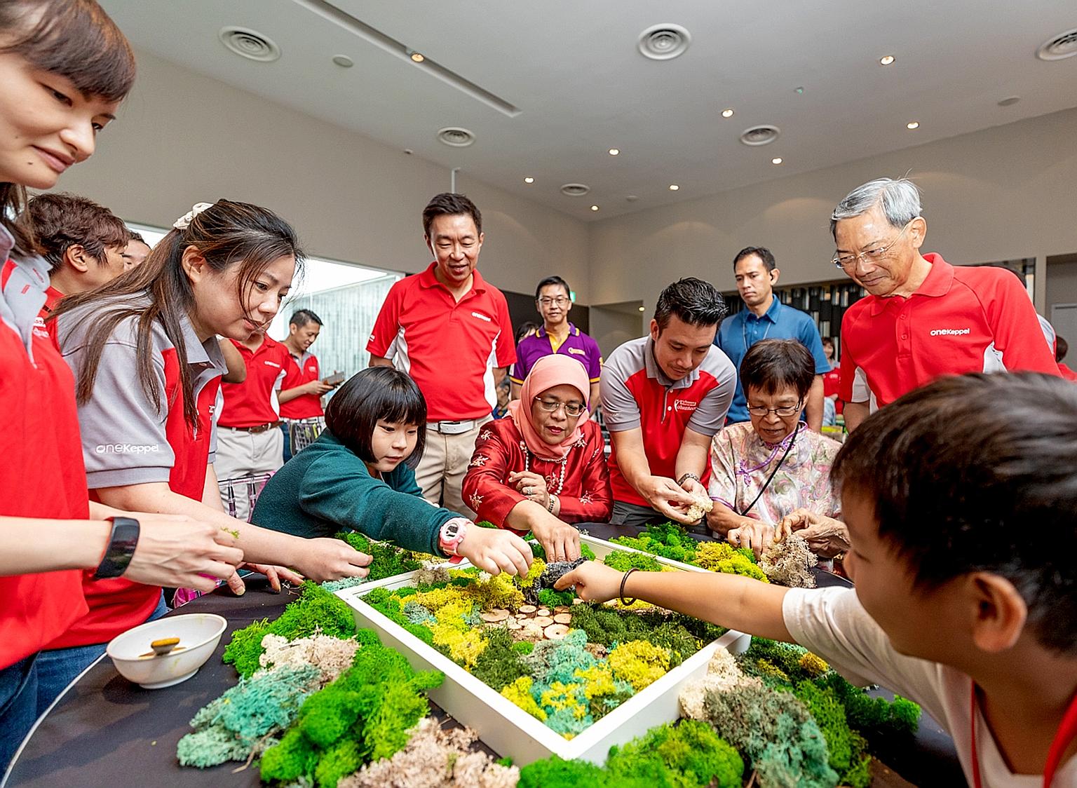 President Halimah Yacob (centre, seated), Keppel Corporation chairman Lee Boon Yang (right, standing) and Keppel CEO Loh Chin Hua (third from left, standing), join Keppel's beneficiaries from Monfort Care and Care Corner in a moss art activity.