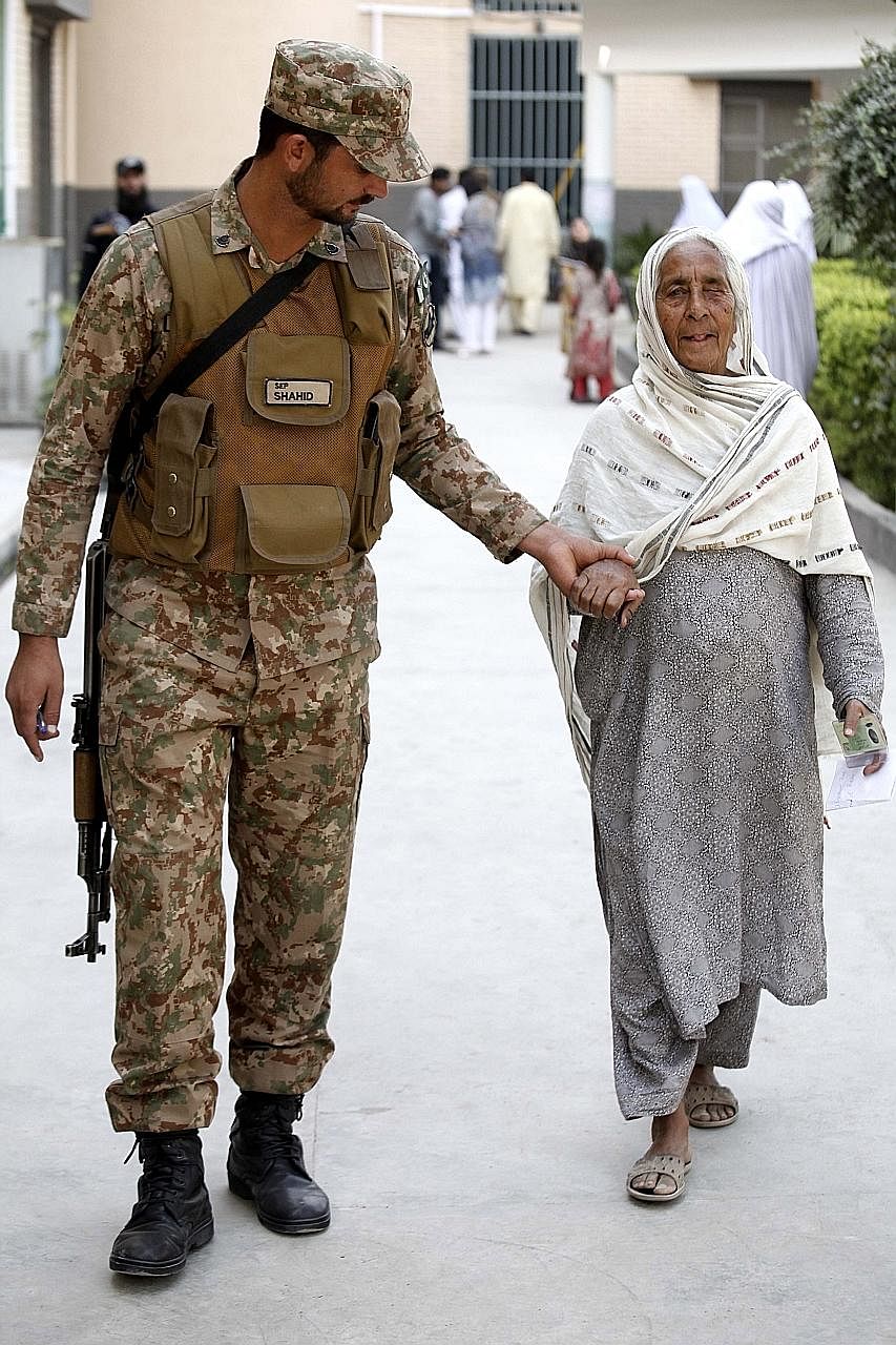 Above: The scene of a suspected suicide bomb attack outside a polling station during general elections in Quetta, Pakistan, yesterday. At least 31 people were killed and many more injured in the incident. Left: An Army soldier helping a woman as she 