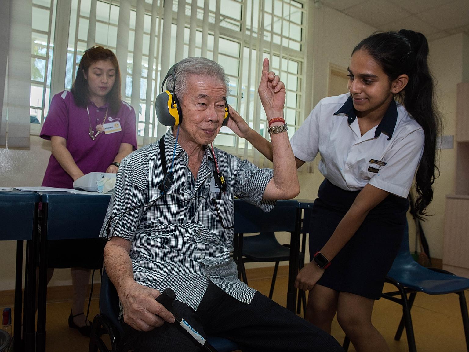 Secondary 2 student Raksha Narayan Rao helping Mr Koh Tiong San, 74, during his hearing check, which was conducted by Ms Mildred Tan (in purple) from a healthcare provider.
