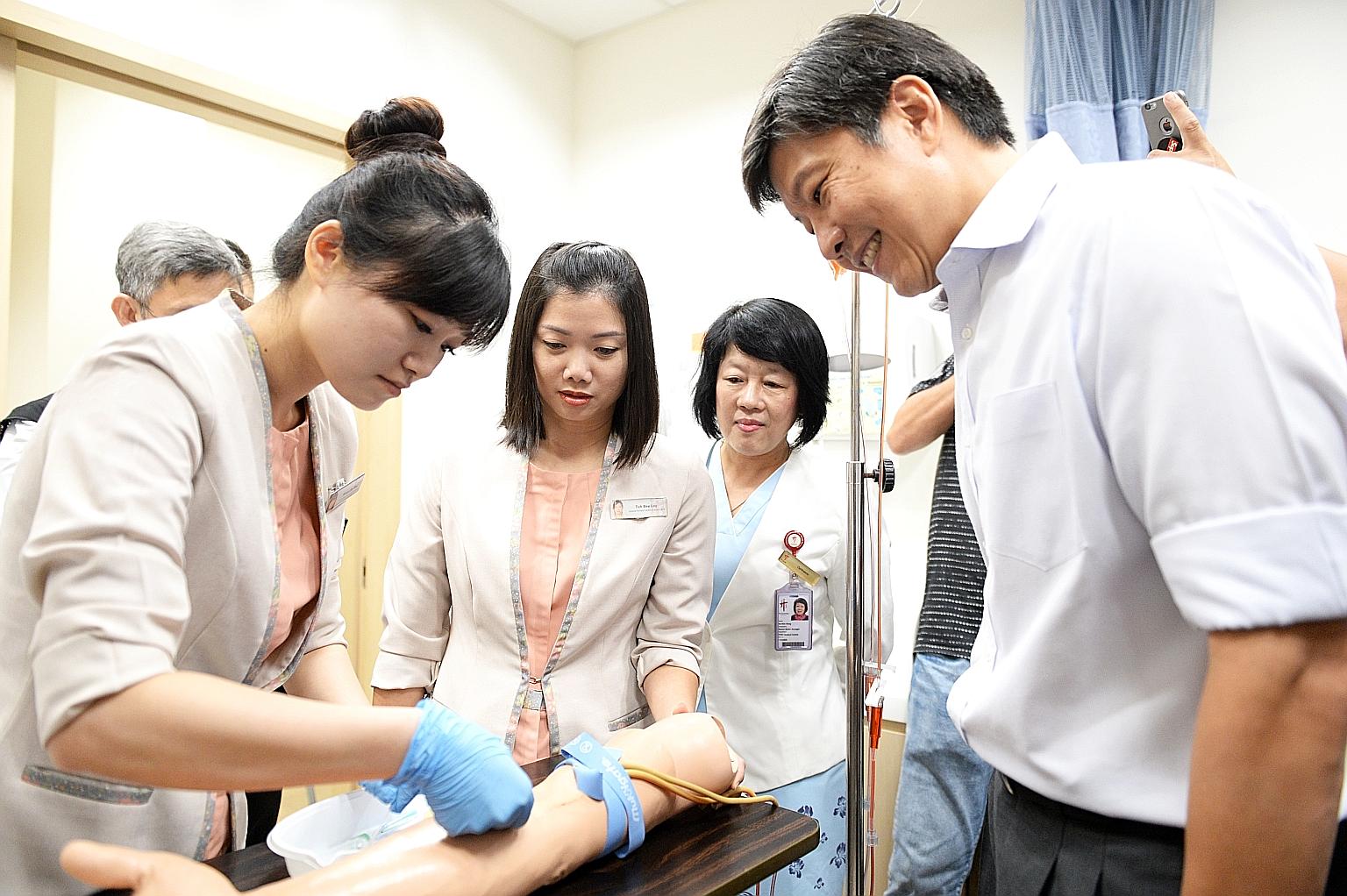 NTUC secretary-general Ng Chee Meng observing TTSH senior patient service associates Woon Shi Mei and Toh Bee Lay demonstrate how to draw blood under the watchful eyes of senior nurse manager Ho Kim Hong.