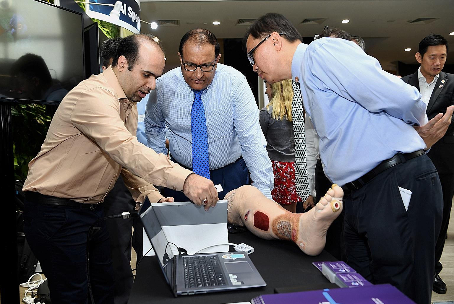 Minister for Communications and Information S. Iswaran (centre) and AI Singapore executive chairman Ho Teck Hua observing a demonstration of artificial intelligence by Dr Hossein Nejati, chief technology officer of health tech start-up KroniKare, whi