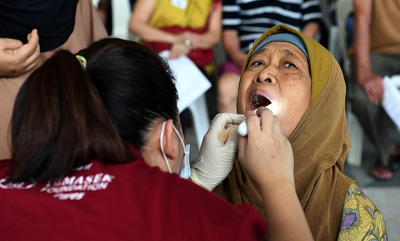 Madam Sudiah Sapii, 76, getting her teeth checked by a volunteer at a health screening yesterday at Kampung Admiralty, where Project Silver Screen was launched. Around 200 people from the neighbourhood took the chance to have their vision, hearing an