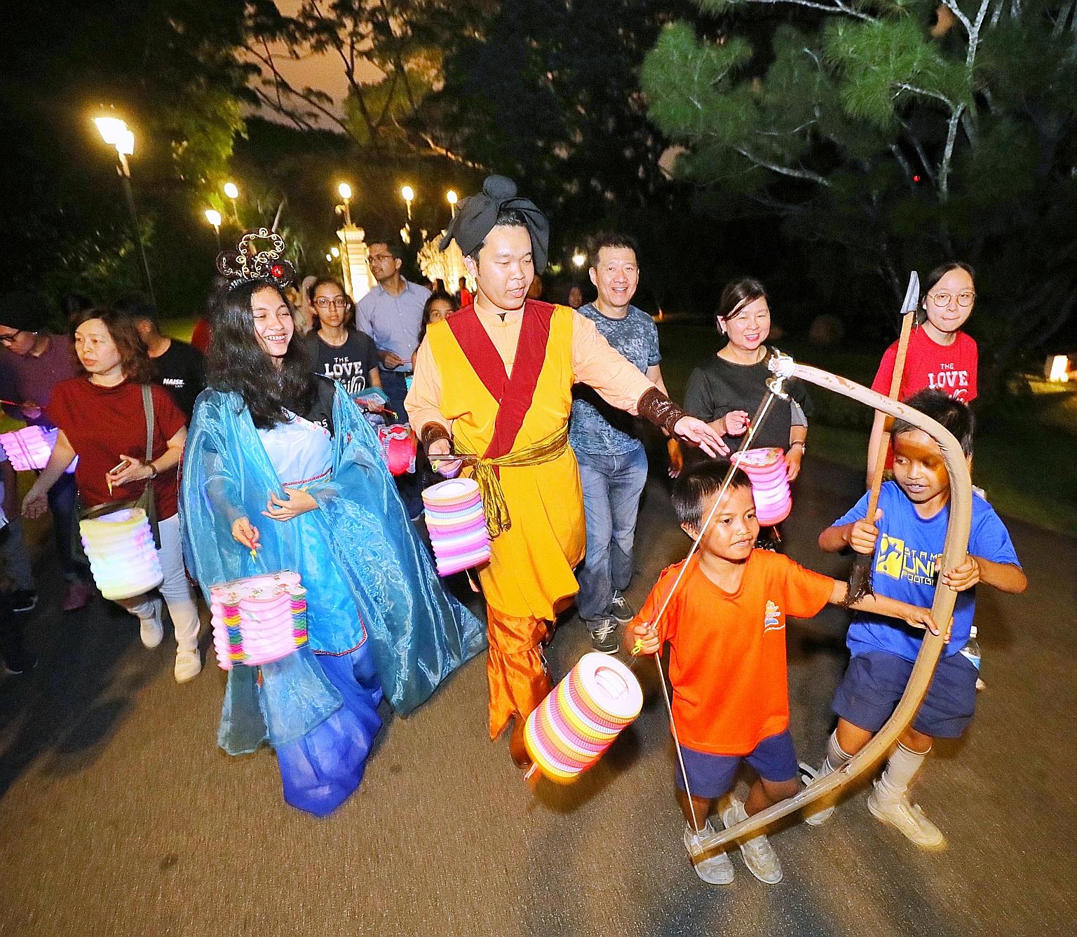 Performers dressed up as Chinese folklore characters Chang Er and Hou Yi leading Ryan Dinzly Naiman (in orange top), nine, Syahfril Hans (in blue top), 10, and other beneficiaries of the President's Challenge for a tour of the Istana grounds yesterda