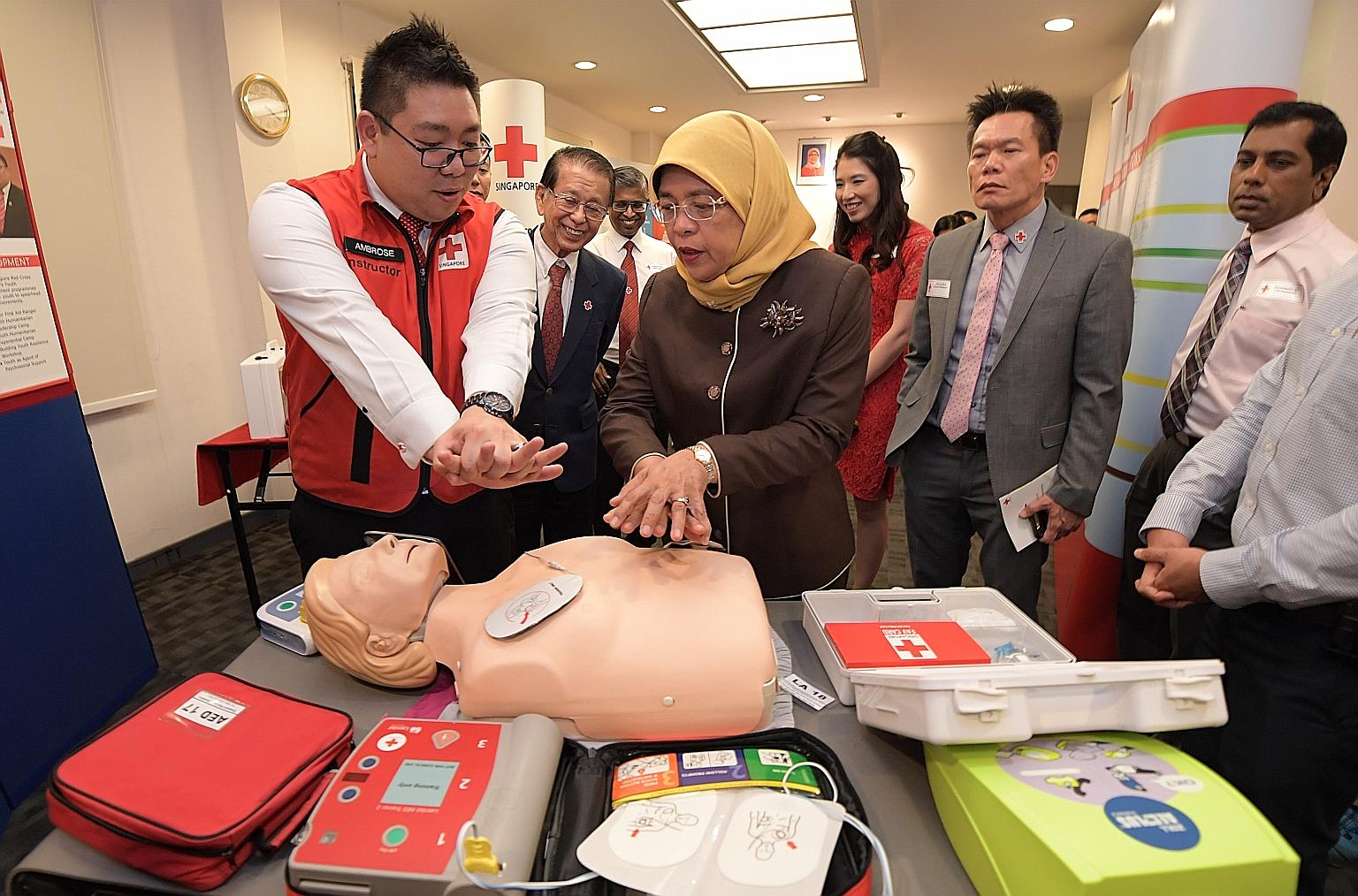 Mr Ambrose Lee (at left), 31, assistant head of the Singapore Red Cross (SRC) Academy, showing President Halimah Yacob how to perform cardiopulmonary resuscitation or CPR on a dummy during her inaugural visit to Red Cross House yesterday. Madam Halim