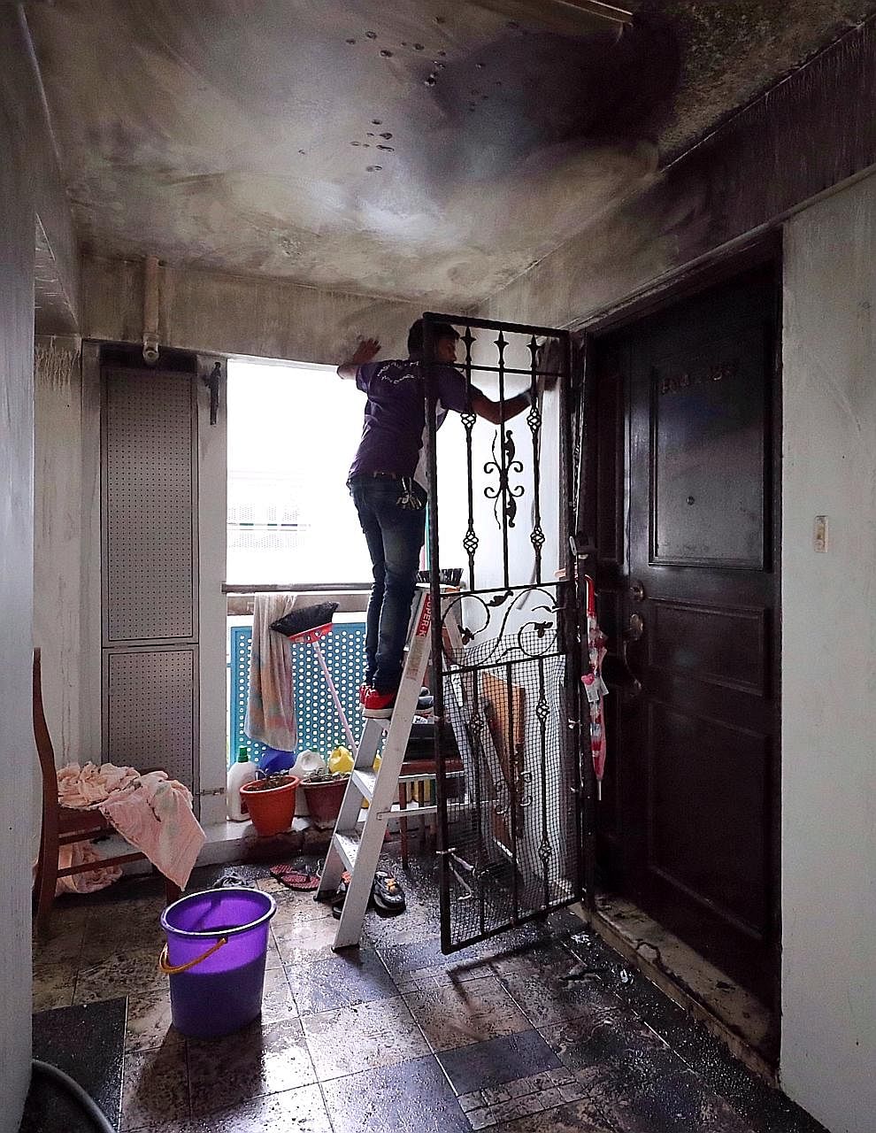 Left: A worker cleaning the blackened walls of the common corridor outside the fourth-floor flat in Block 163B, Punggol Central, that caught fire yesterday. Above: Madam Maimon Sharif, who died in the blaze, was believed to be making lunch for her gr