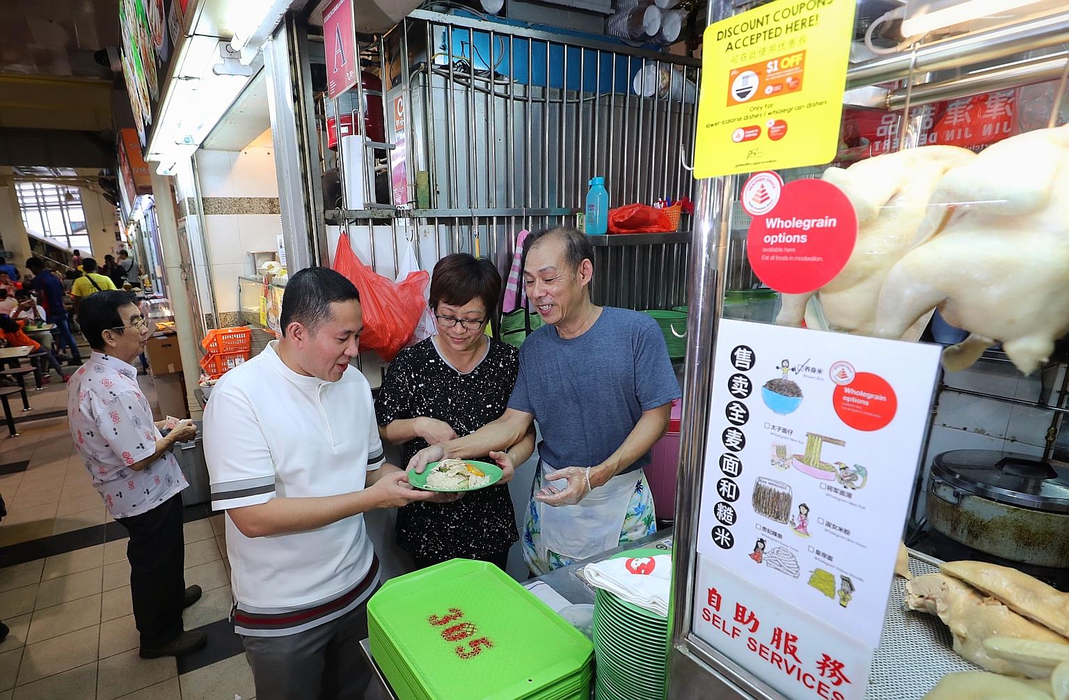 Uncle Jack Hainance Boneless Chicken Rice owner Jack Toh, 54, and his wife Sally Nyo, 52, showing Senior Parliamentary Secretary for Health and Home Affairs Amrin Amin a plate of whole grain chicken rice from their stall. The Health Promotion Board a