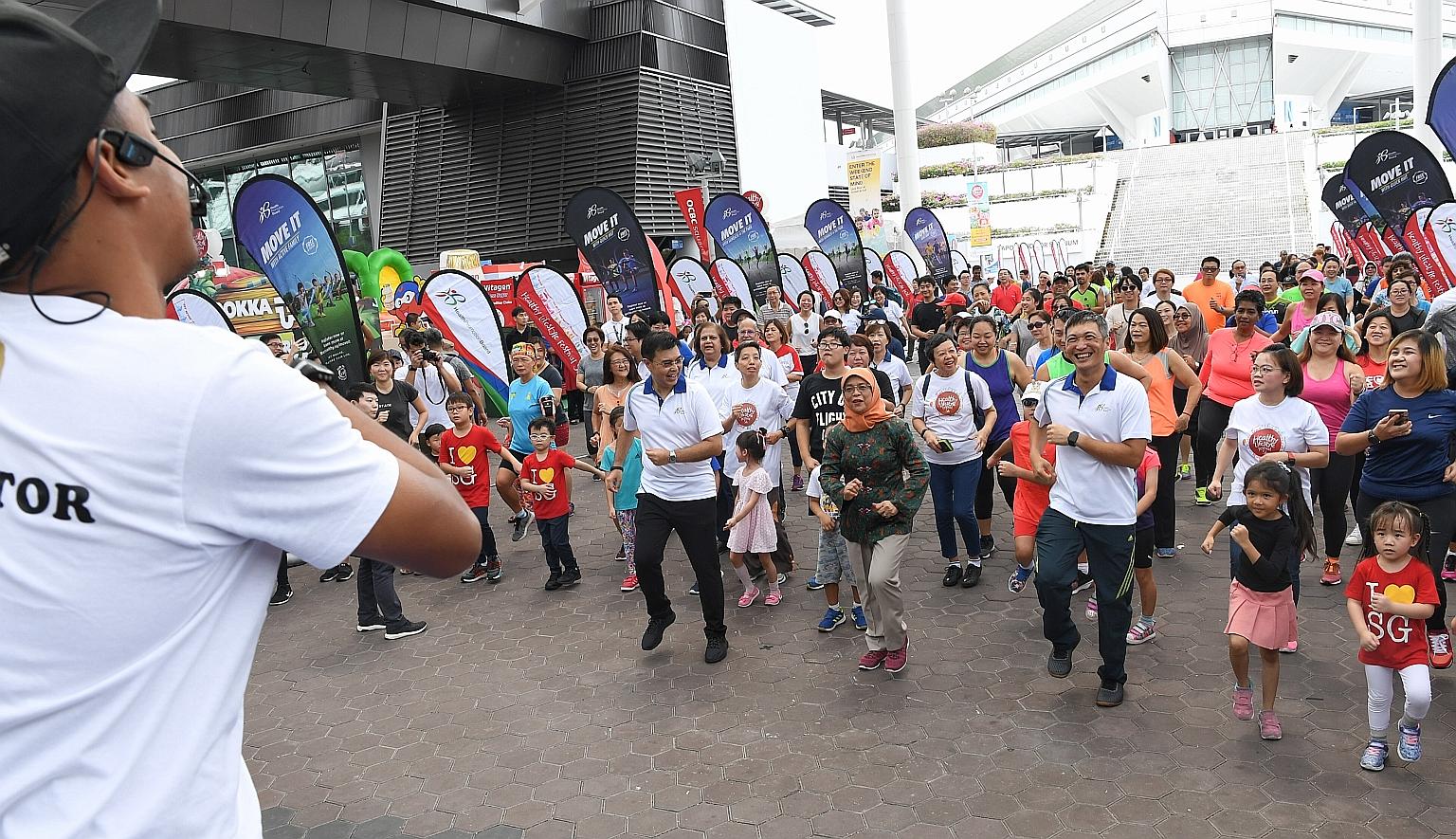 President Halimah Yacob, flanked by HPB chairman Philip Lee (left) and the board's CEO Zee Yoong Kang, doing the Greater Singapore Workout together with an enthusiastic crowd at the Singapore Sports Hub yesterday.