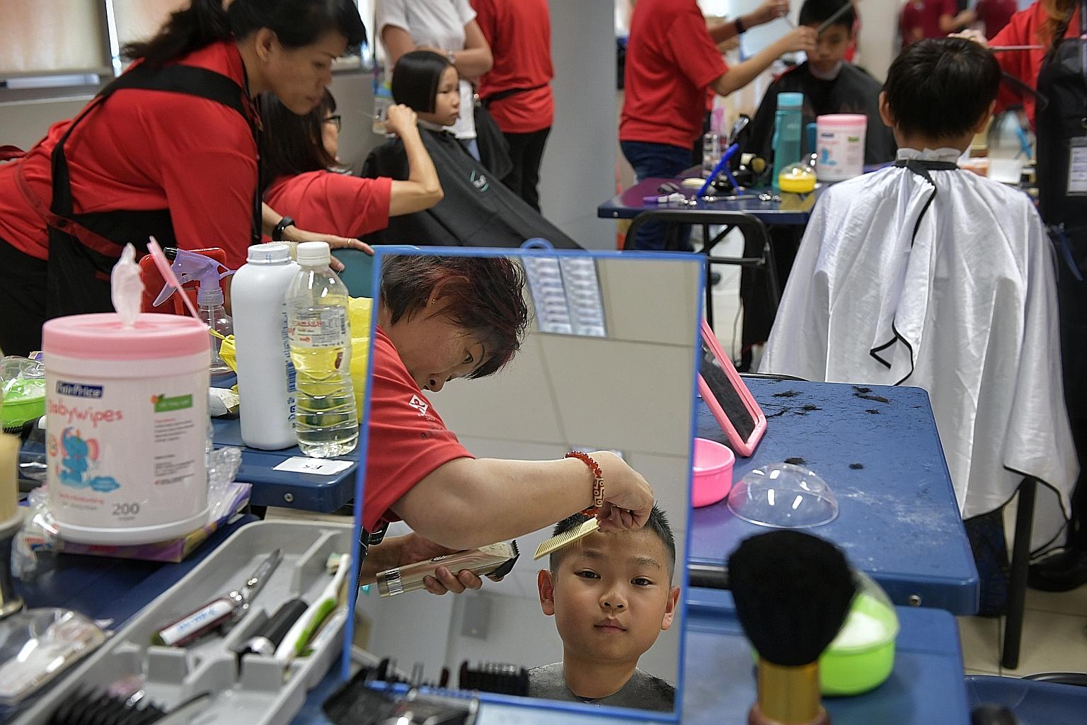 Tnee Yu, 10, getting a free haircut at the CDAC Ready for School event at Nanyang Junior College yesterday. Some 6,500 low-income families received family and school-ready packs containing vouchers at the event.