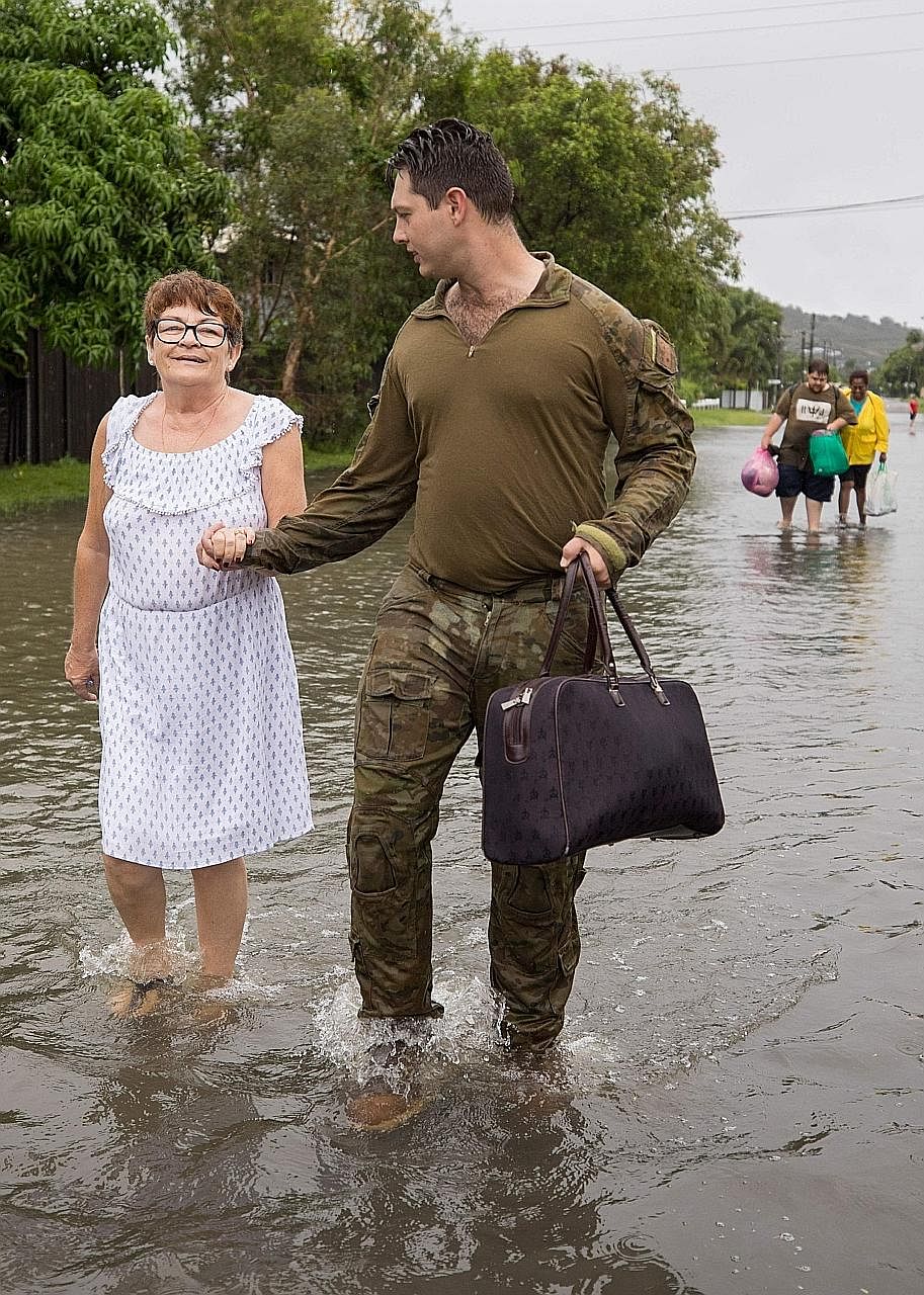 (Above) Gunner Tavis McEwan from the Royal Australian Artillery helping to evacuate a resident from her home amid the rising floodwaters in Townsville. (Left) A crocodile spotted on the streets in Townsville yesterday. A photo from the Queensland Fir