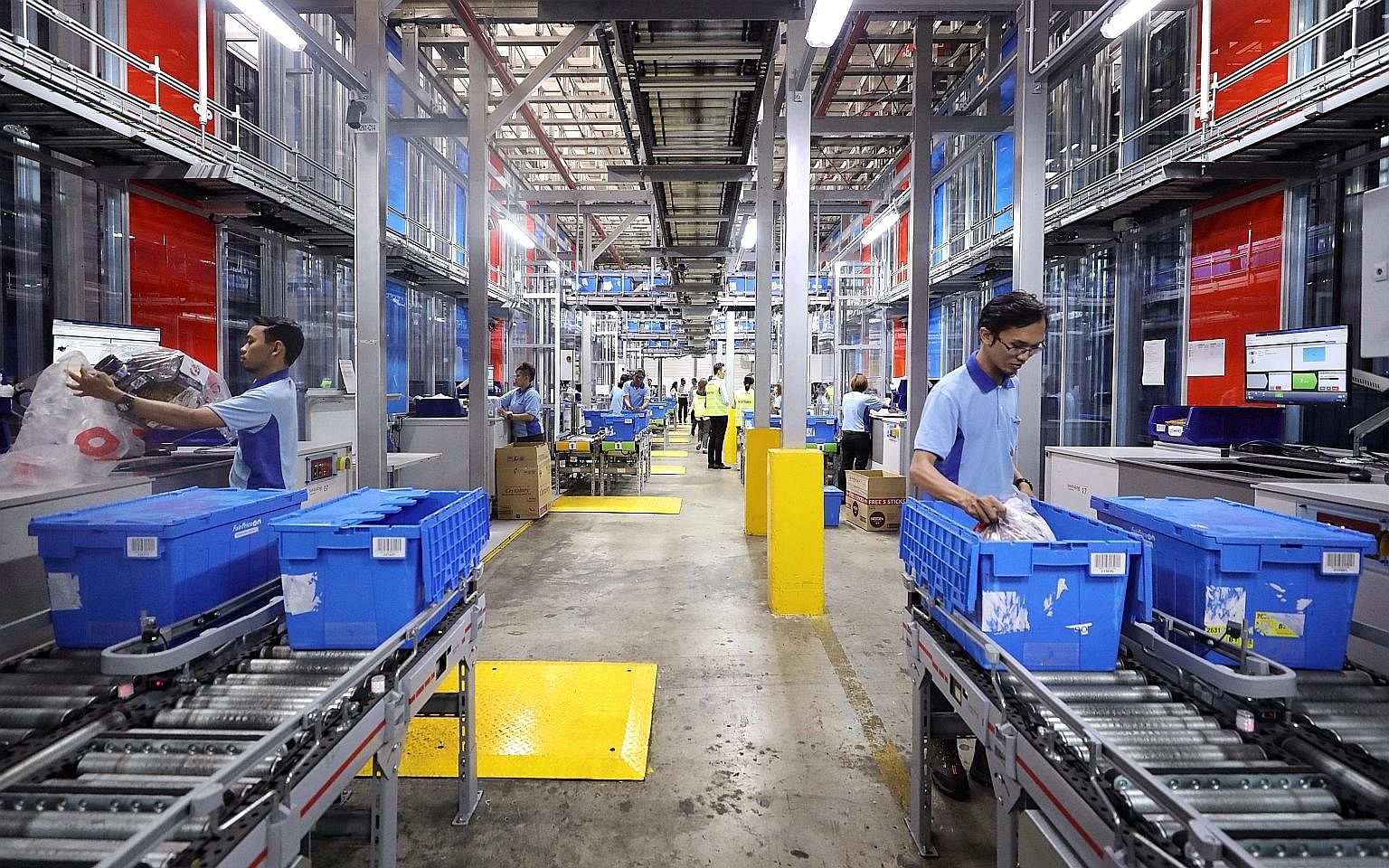 Pickers at FairPrice distribution centre retrieving ordered items from storage bins brought to them by AutoStore robots. FairPrice's training has helped workers quickly pick up new skills to make use of the new systems, and their work environment is 