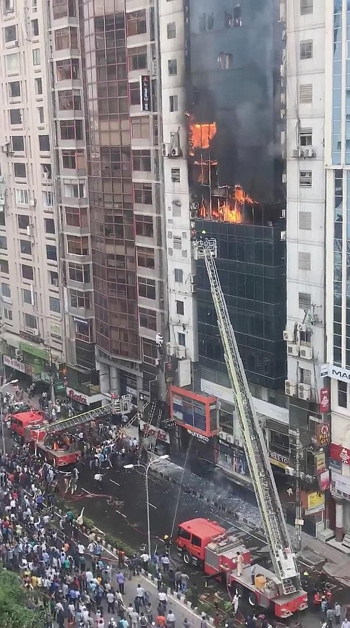Firefighters rescuing a person from the burning office building in Bangladesh's capital city. A person trying to climb down Dhaka's FR Tower to escape a fire which broke out inside the building yesterday. A large crowd outside the 22-storey office bu