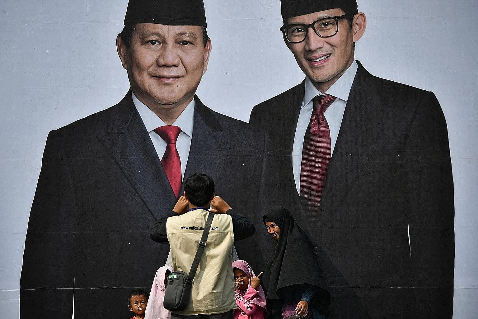 Supporters of presidential hopeful Prabowo Subianto taking pictures in front of a poster of him (left) and his running mate Sandiaga Uno at the Gelora Bung Karno Stadium yesterday, a day ahead of his mega rally there.