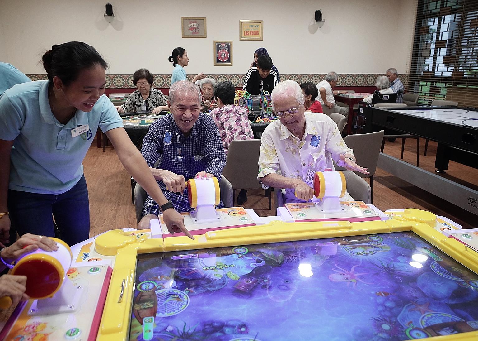Retiree Robin Liow (centre), 72, who has Parkinson's disease and suffered a hip fracture last year, playing an arcade game with fellow retiree Teo Cheng Lok, 85, in the games room at the senior care centre in Ghim Moh. They are guided by Ms Moh Moh, 